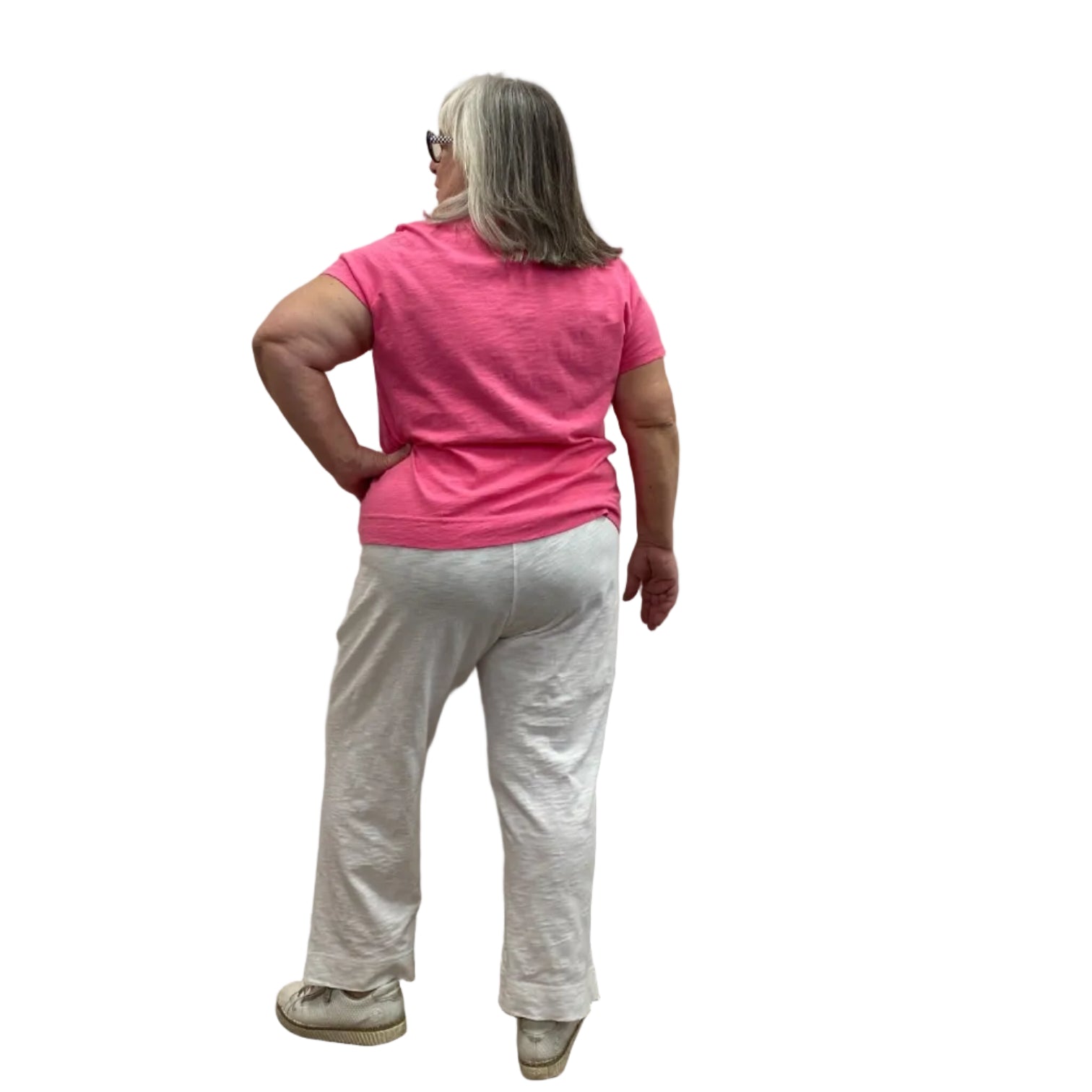 Woman wearing the Escape V Neck Tee in Cosmo Pink with a white heart shape on the front, paired with white pants, against a white background.