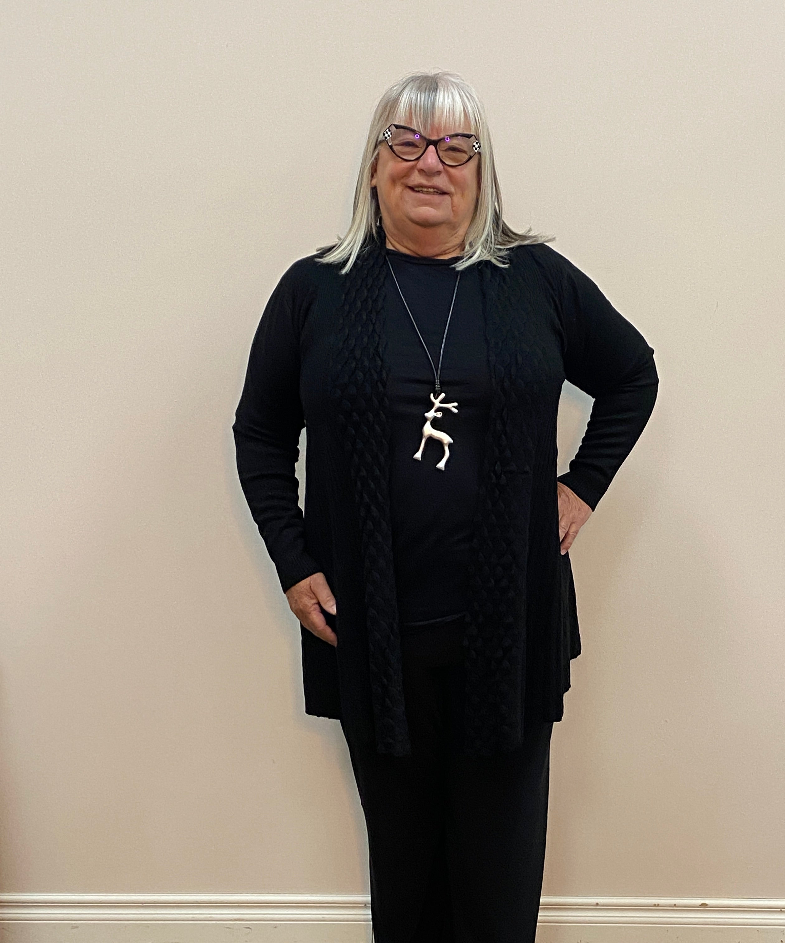 Person wearing a black outfit with a white wall and wooden floor background