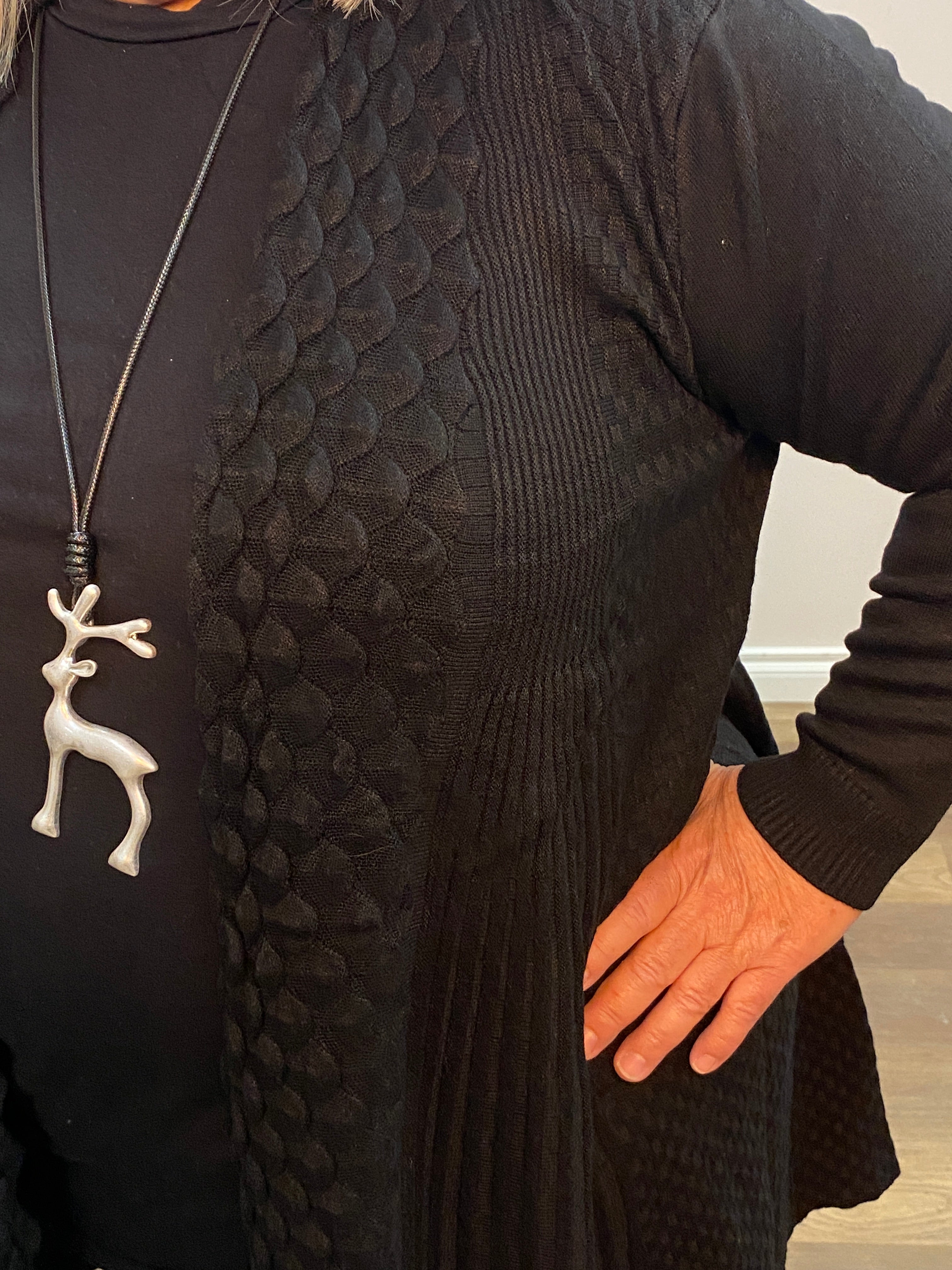 Person wearing a textured black garment with a hand on the fabric, against a neutral background.