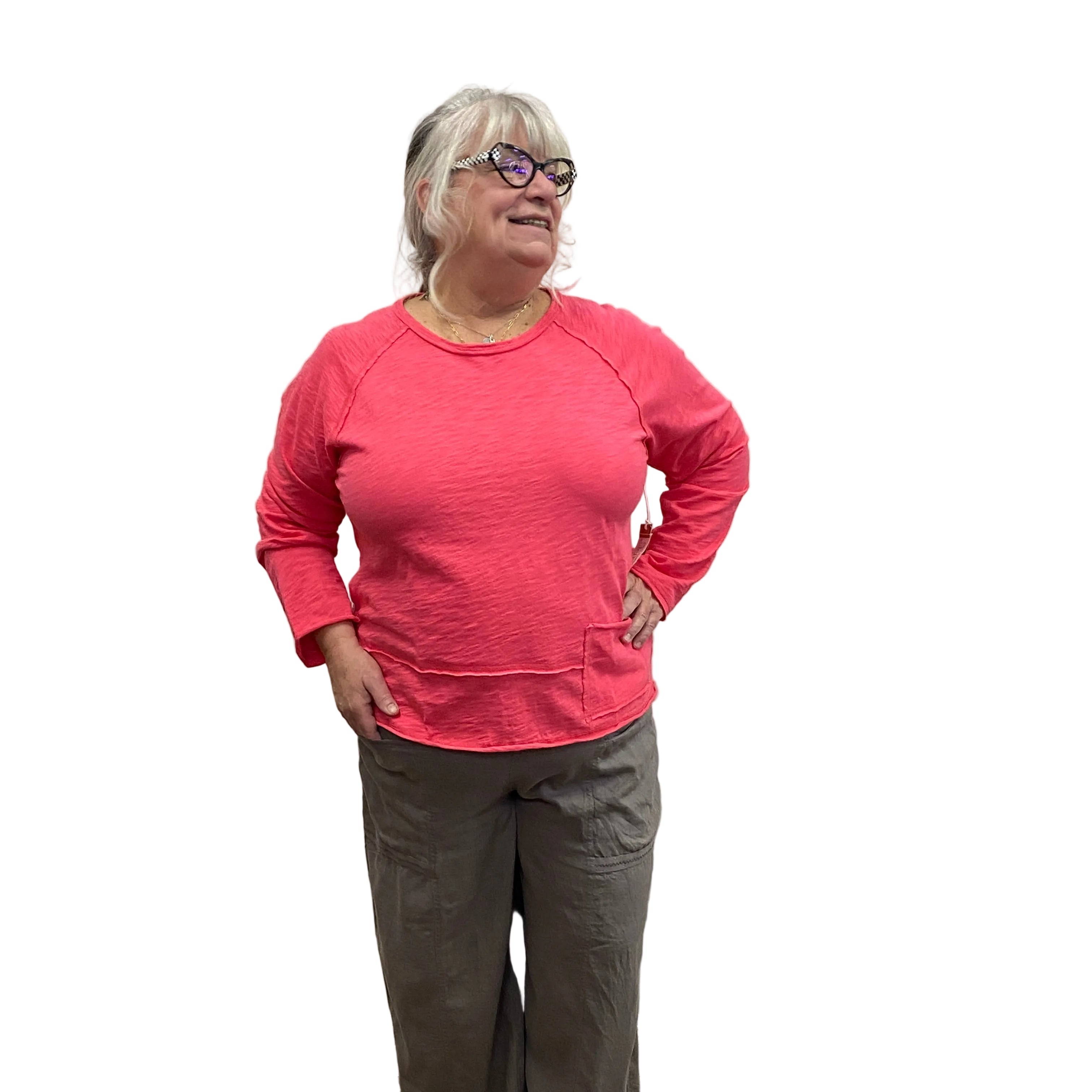 Person wearing a pink sweatshirt and dark pants standing against a white wall with a wooden floor.