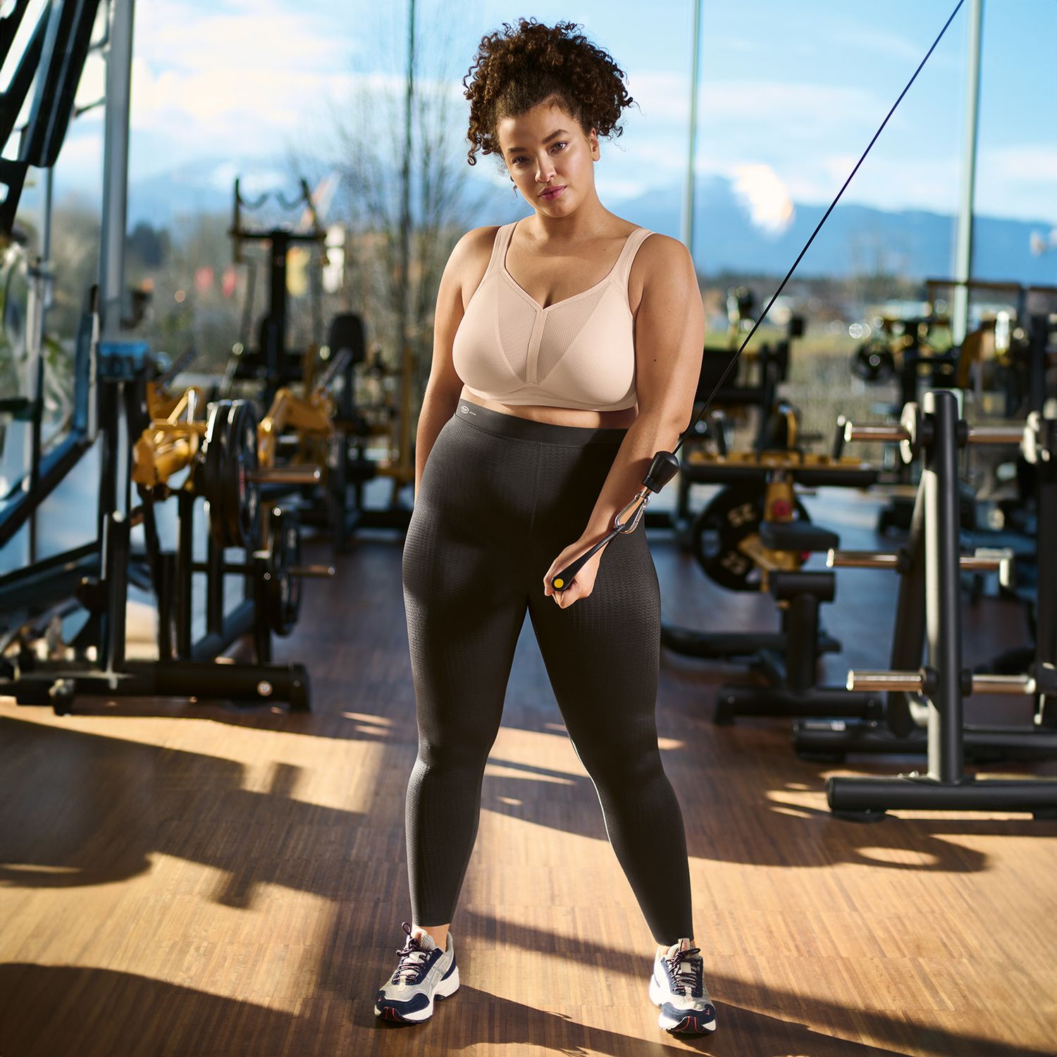 Woman exercising in a gym with equipment and large windows in the background