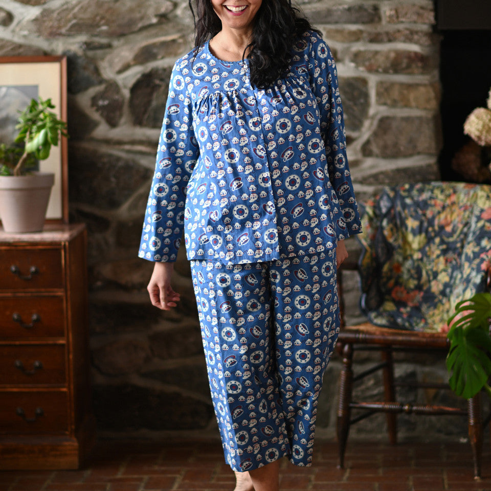 A woman wearing a blue pajama set against a grey wall.