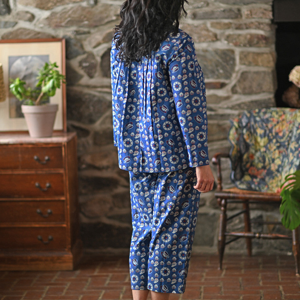 A woman wearing a blue pajama set against a grey wall.