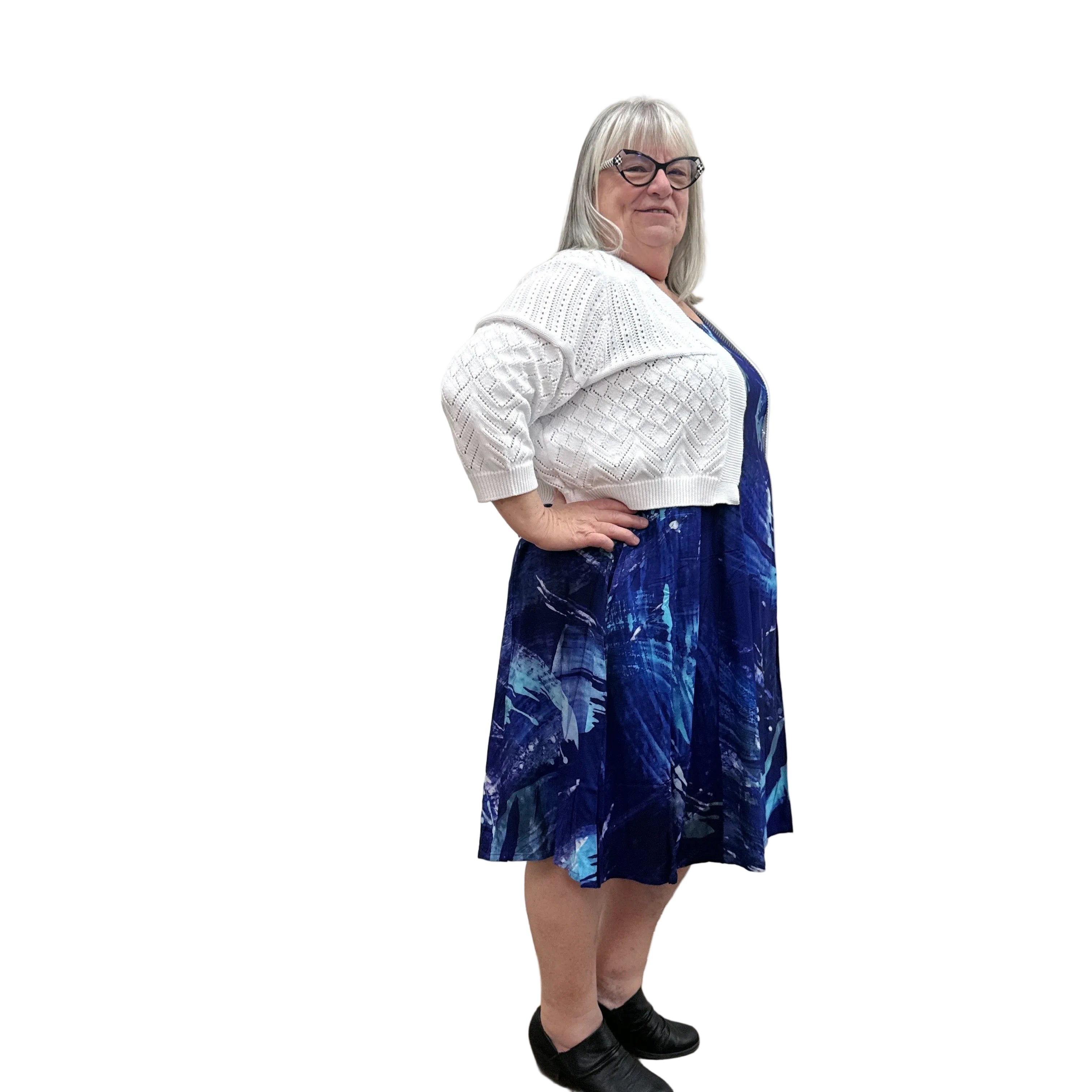 Woman wearing a white Blue Sky Aldi Sweater over a blue patterned dress on white background.