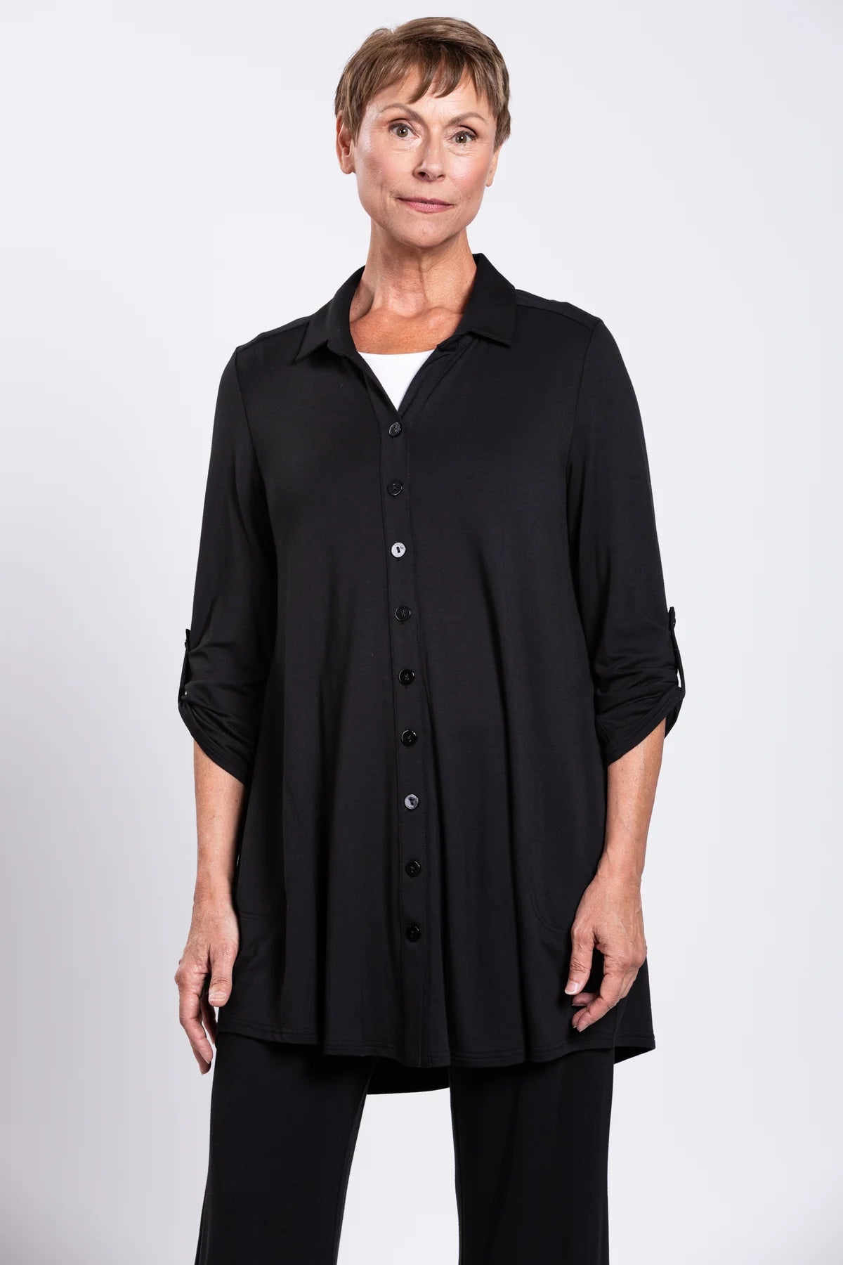 Woman wearing a black button-up shirt and black pants on a white background