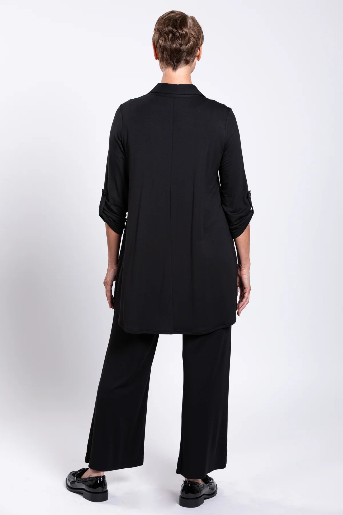 Person wearing a black outfit with a long shirt and wide-leg pants on a white background