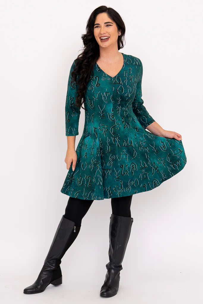 Woman wearing a green patterned dress with black knee-high boots on a white background