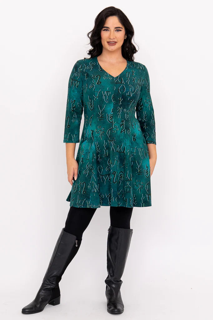 Woman wearing a teal dress with black pattern and black boots on a white background