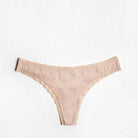 This image displays a delicate and sleek microfiber thong panty, presented in a subtle shade of peach. The design features a low-rise cut with a comfortable fit and back shirring for added stability.
