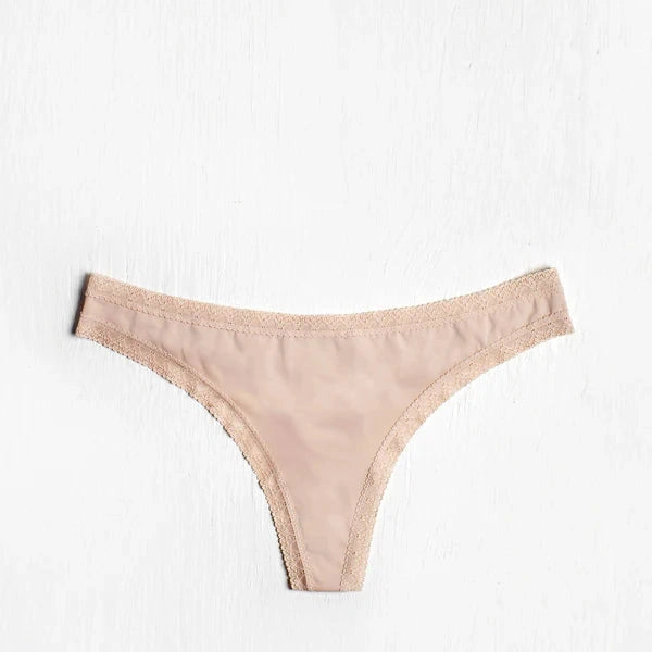 This image displays a delicate and sleek microfiber thong panty, presented in a subtle shade of peach. The design features a low-rise cut with a comfortable fit and back shirring for added stability.