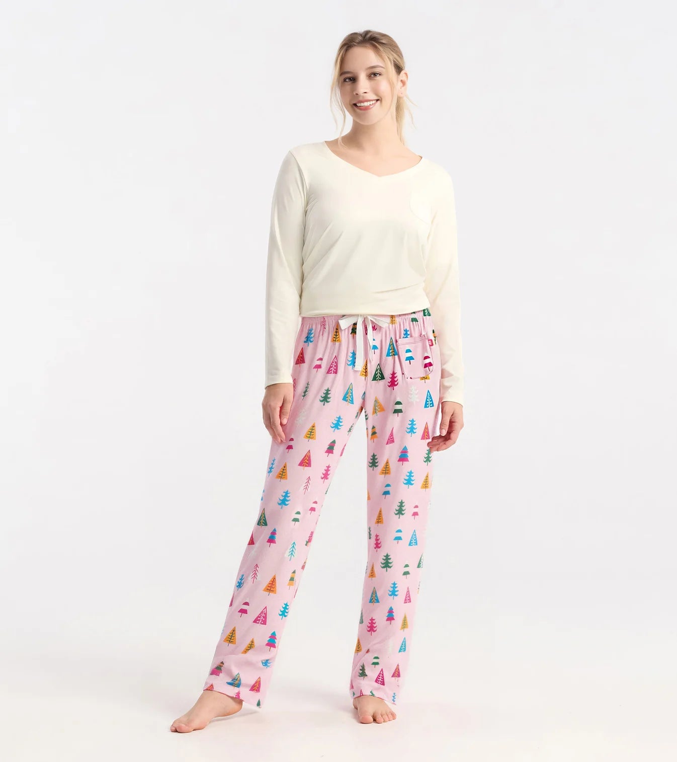 Woman wearing a cream long-sleeve top and pink pajama pants with colorful patterns on a white background