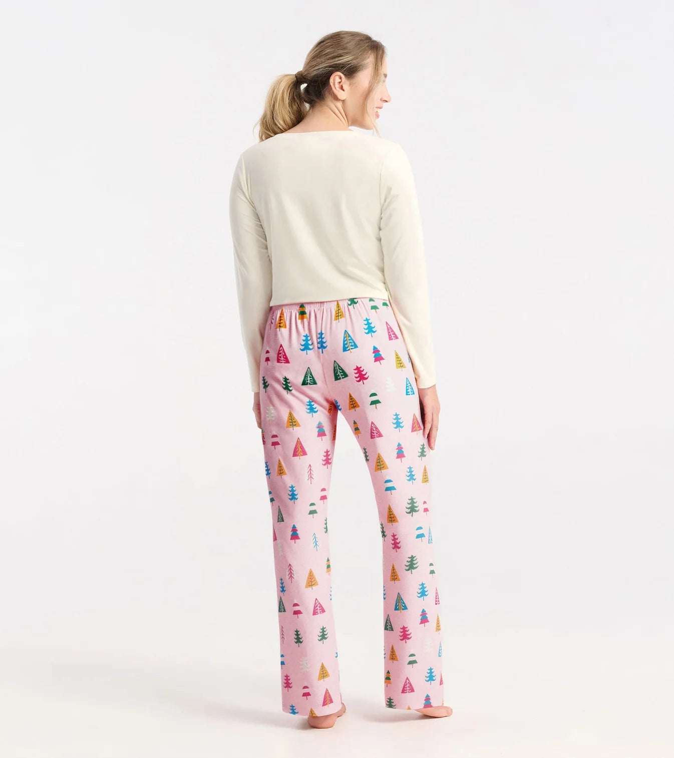 Woman wearing pink pajama pants with tree pattern and cream top on white background