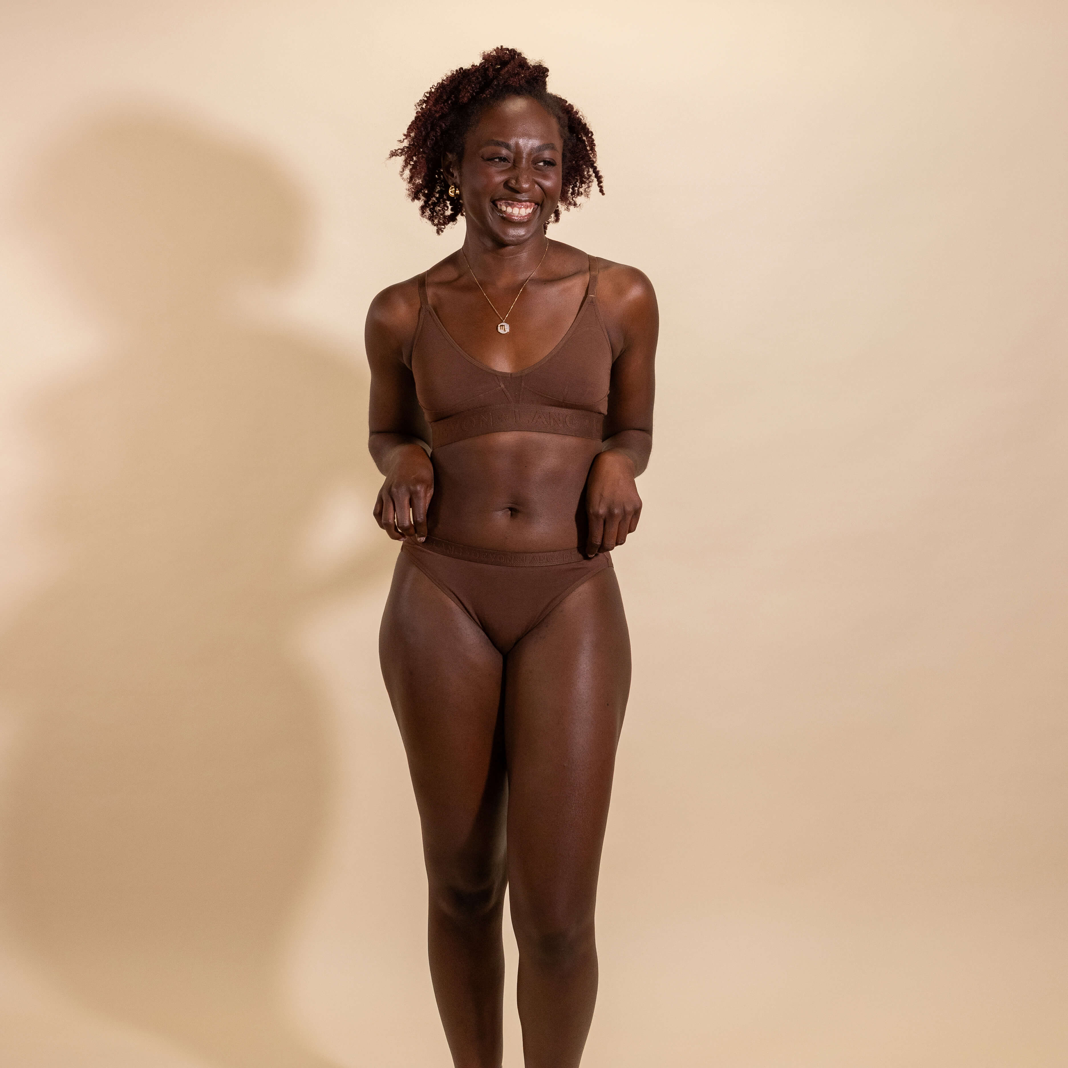 Woman wearing a brown underwear set against a beige background