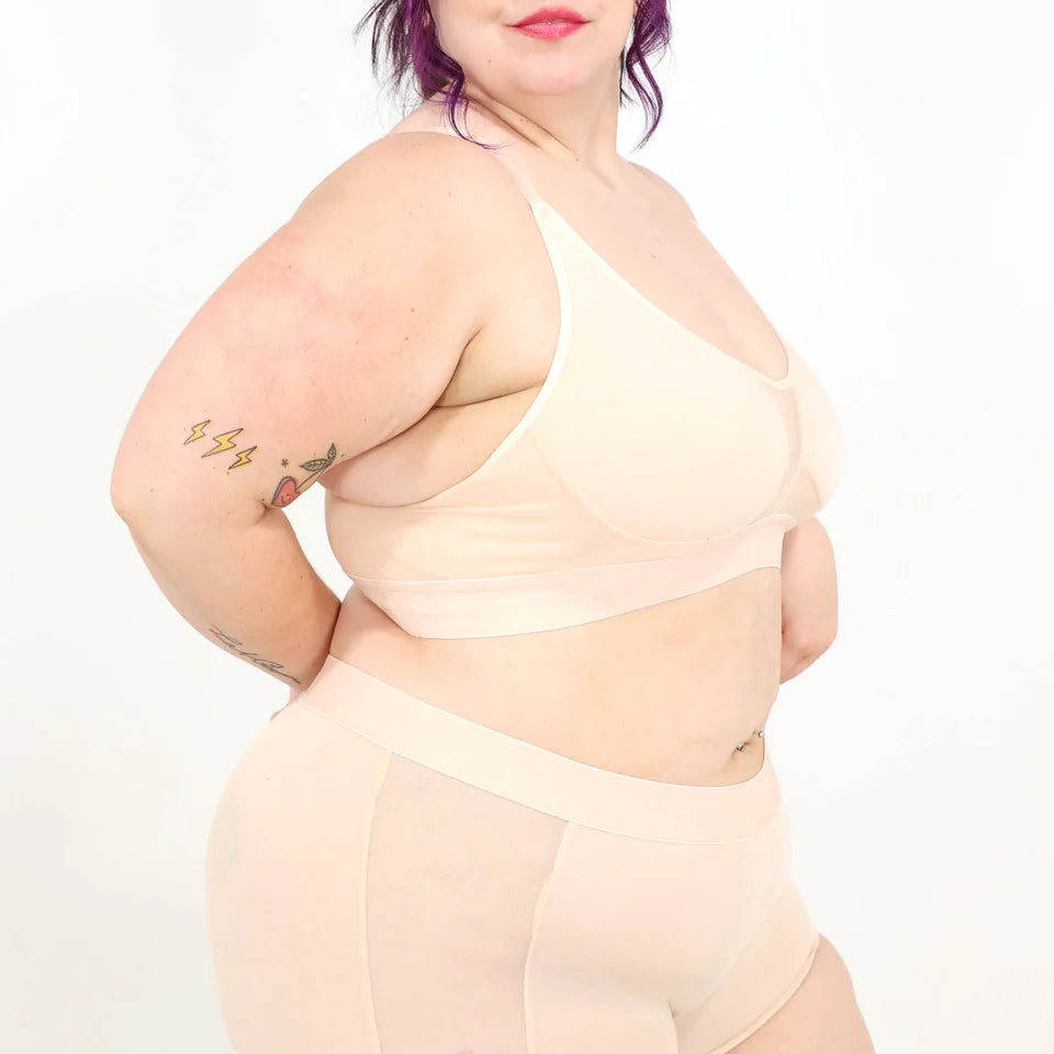 A woman wearing a beige bra and underwear set against a white background