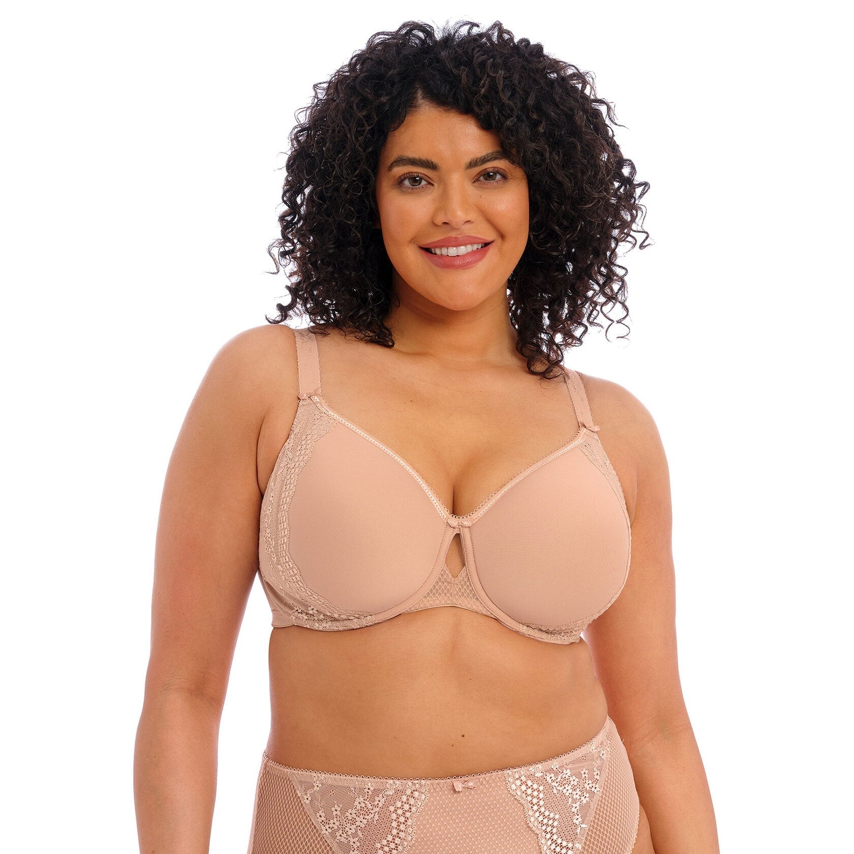 A woman wearing a beige bra and panty set with lace detail against a white back ground.