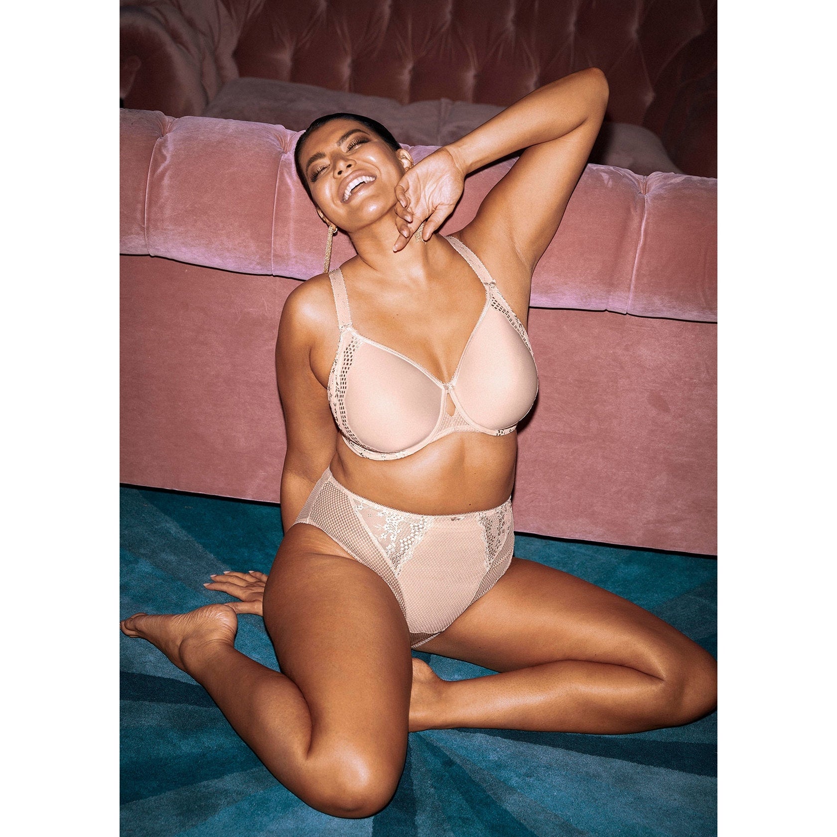 A woman sitting in a room wearing a beige bra and panty set with lace details.