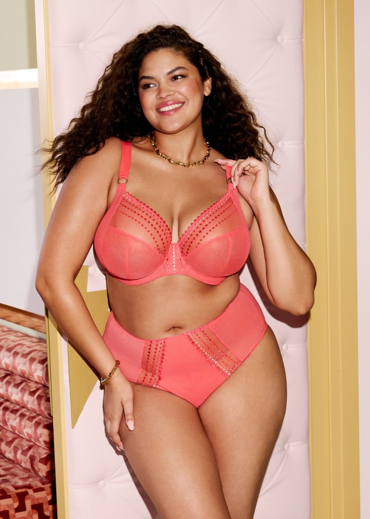 Woman wearing a coral bra and panties set against a light-colored wall.