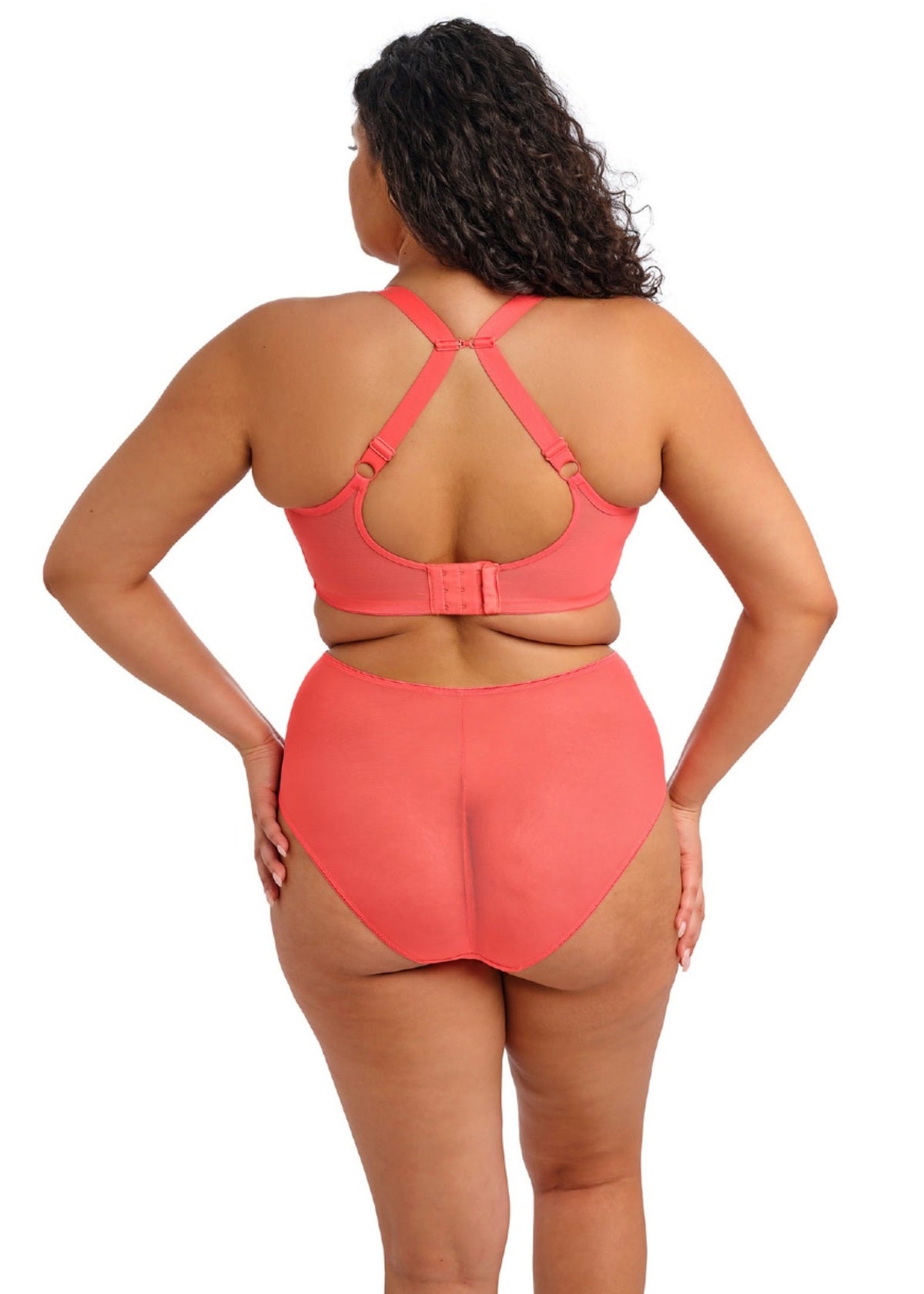 Woman wearing a coral bra and panty set standing backward on a white background