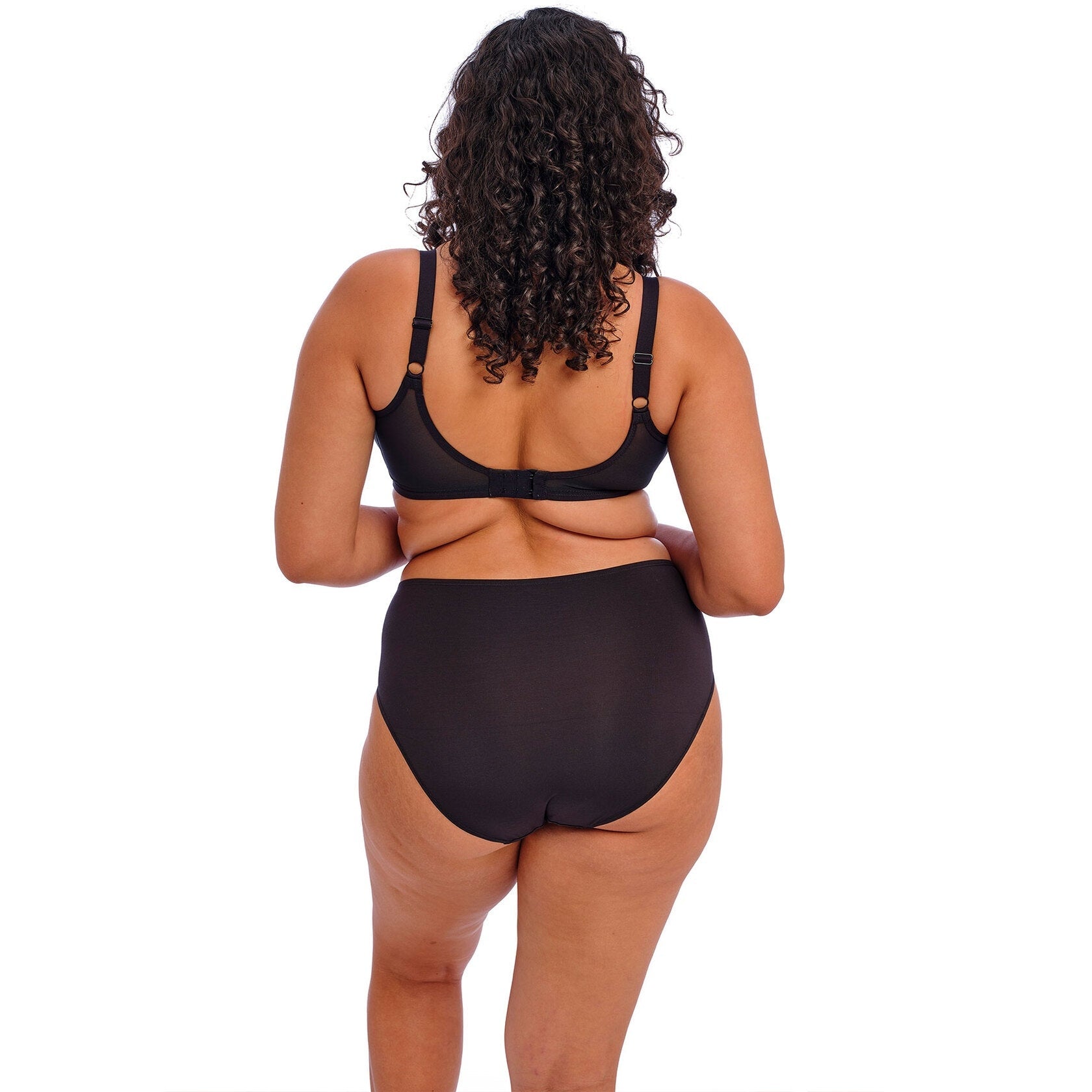 A person wearing a black bra and panty set against a white back ground.