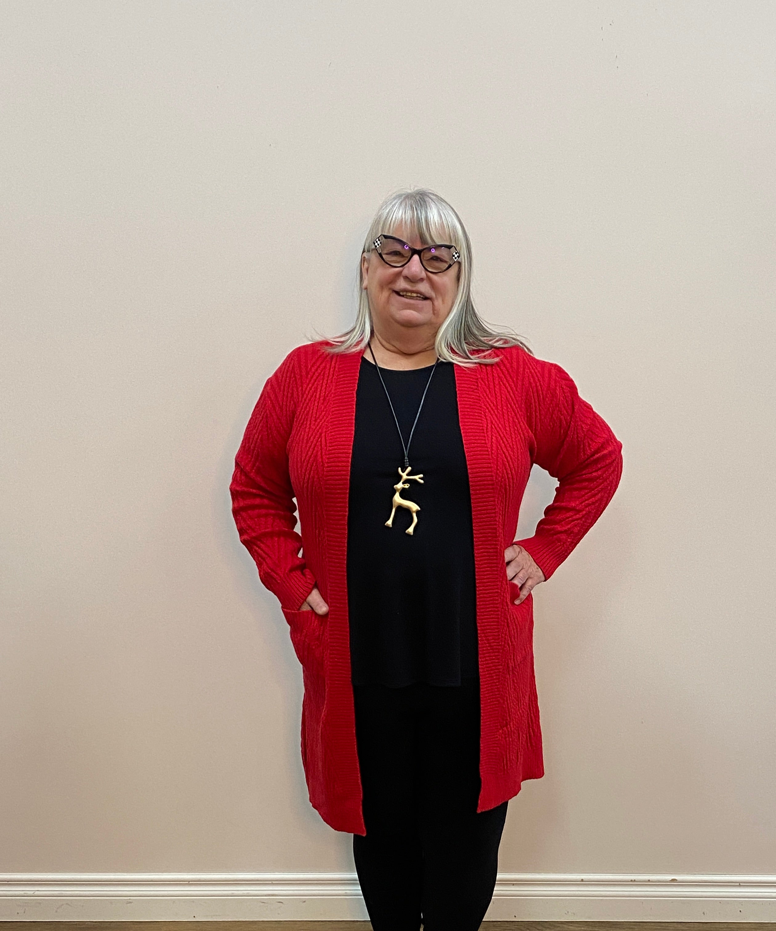 Person wearing a red cardigan and black pants standing on a wooden floor.