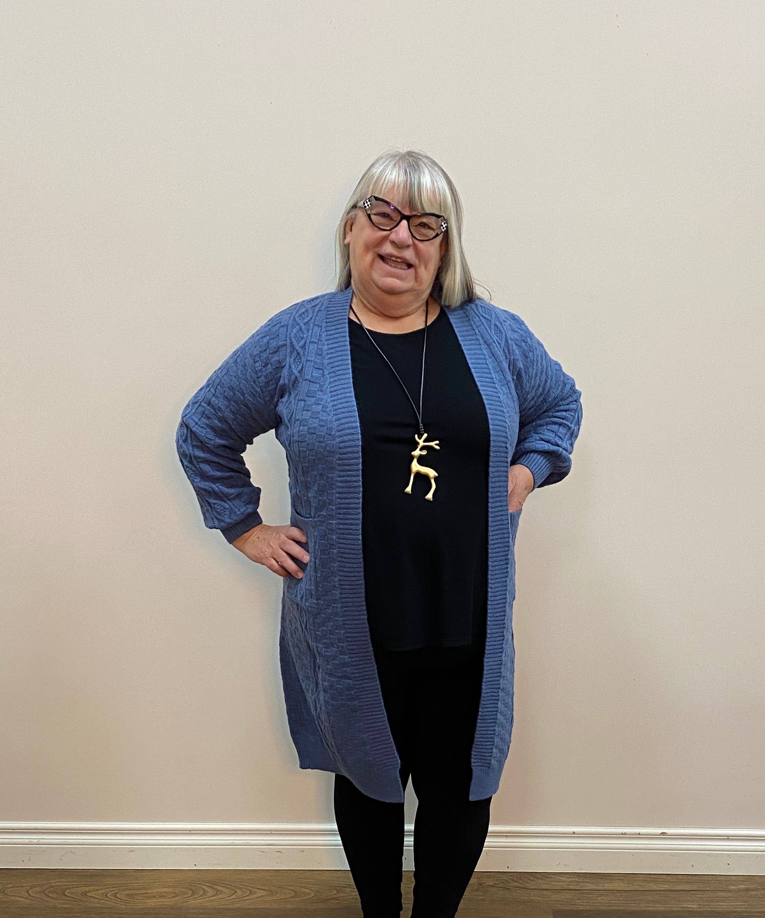 Person wearing a blue sweater and black pants standing on a wooden floor.