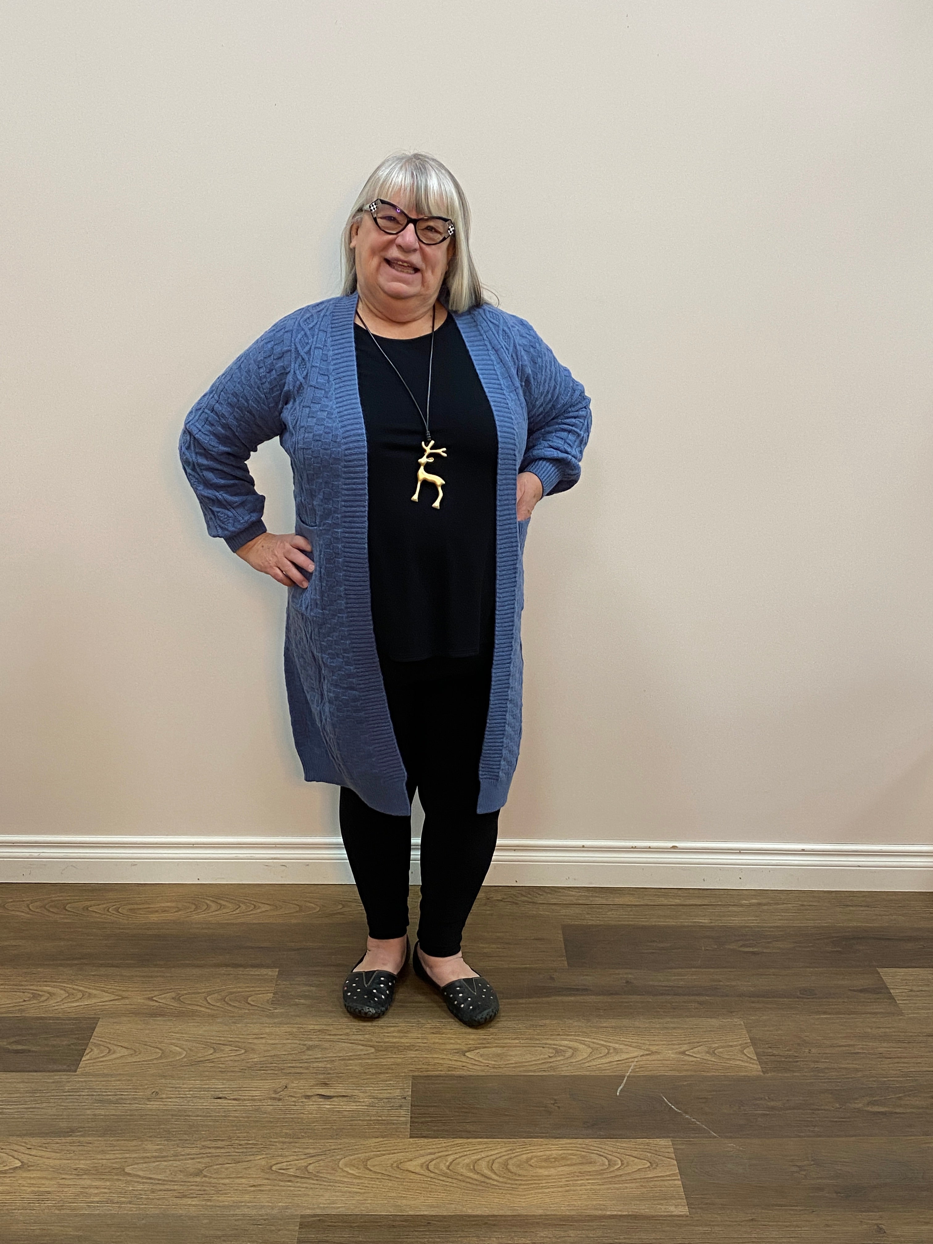 Person wearing a blue sweater and black pants standing on a wooden floor.