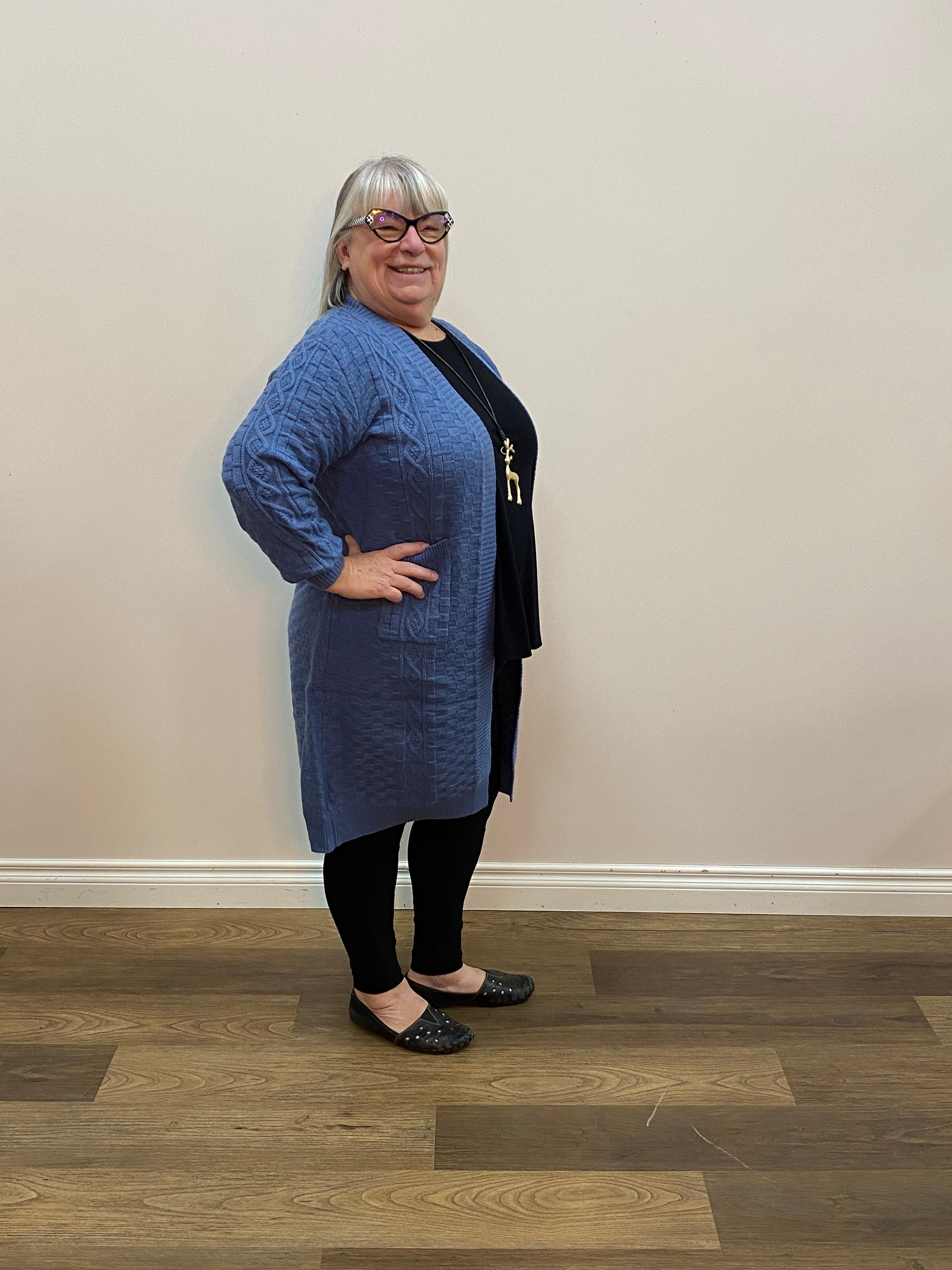 Person wearing a blue cardigan and black pants standing on a wooden floor.