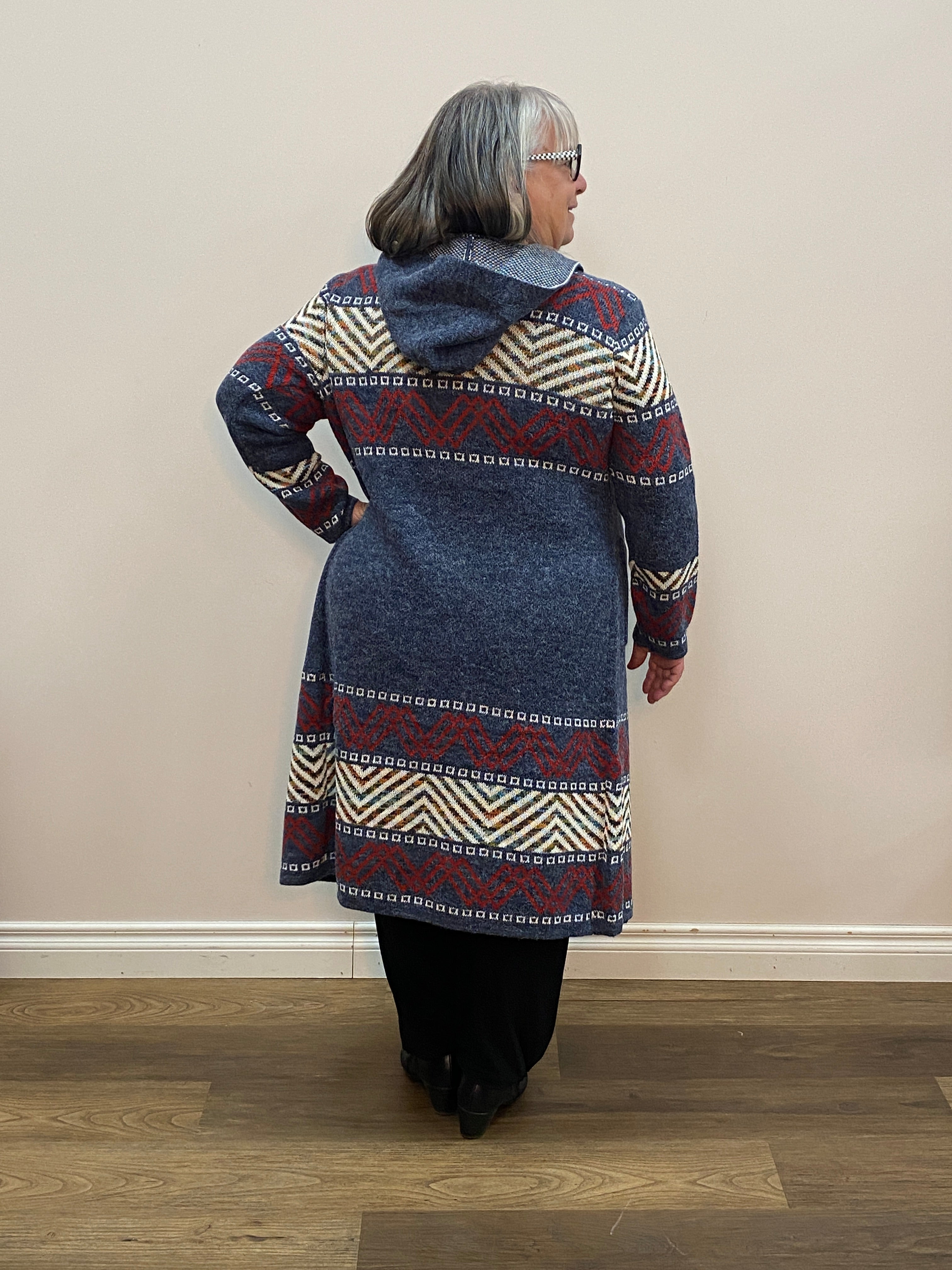 Person wearing a patterned sweater standing against a plain wall.