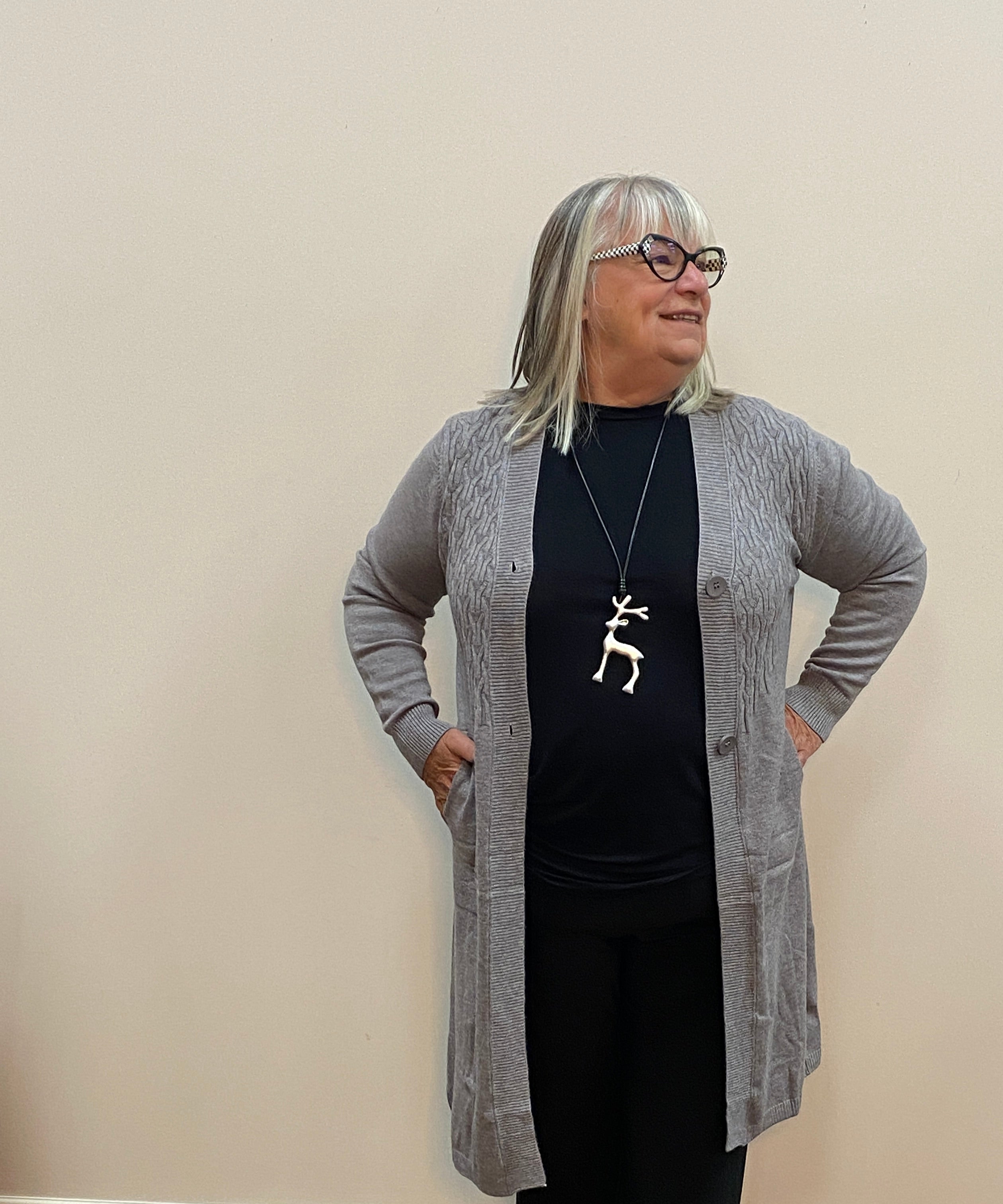 Person wearing a gray cardigan, black top, and black pants in a room with a wooden floor and white walls.
