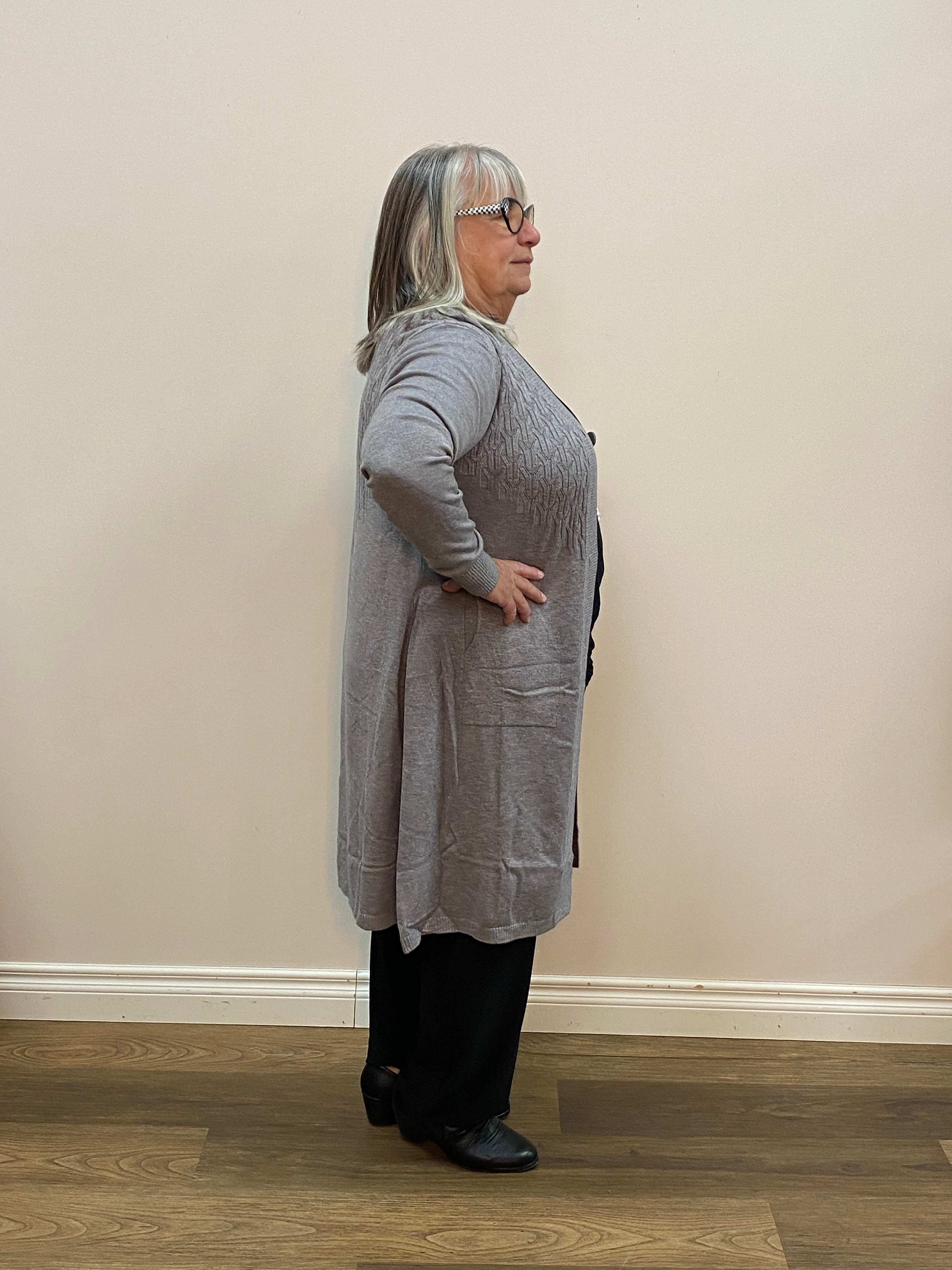 Person wearing a gray outfit standing against a plain wall.