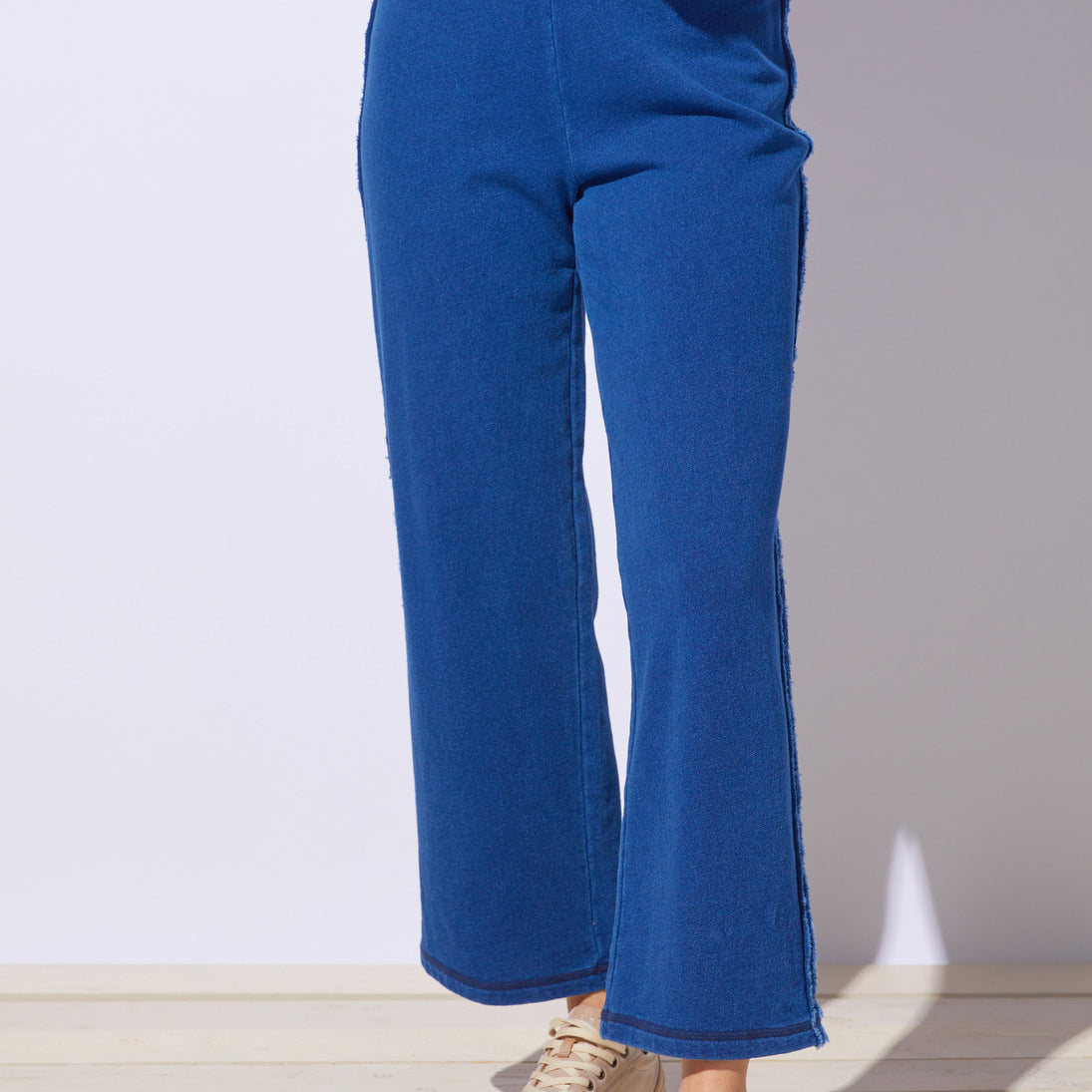 Person wearing blue pants and beige sneakers on a light wooden floor with a white wall background