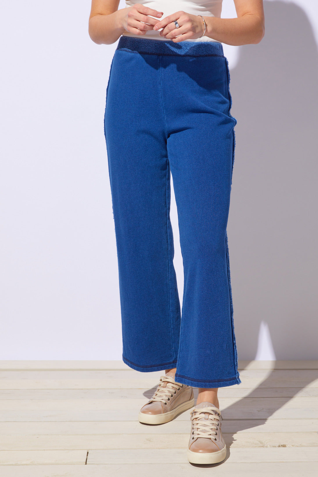 Person wearing blue pants and beige sneakers on a light wooden floor with a white wall background