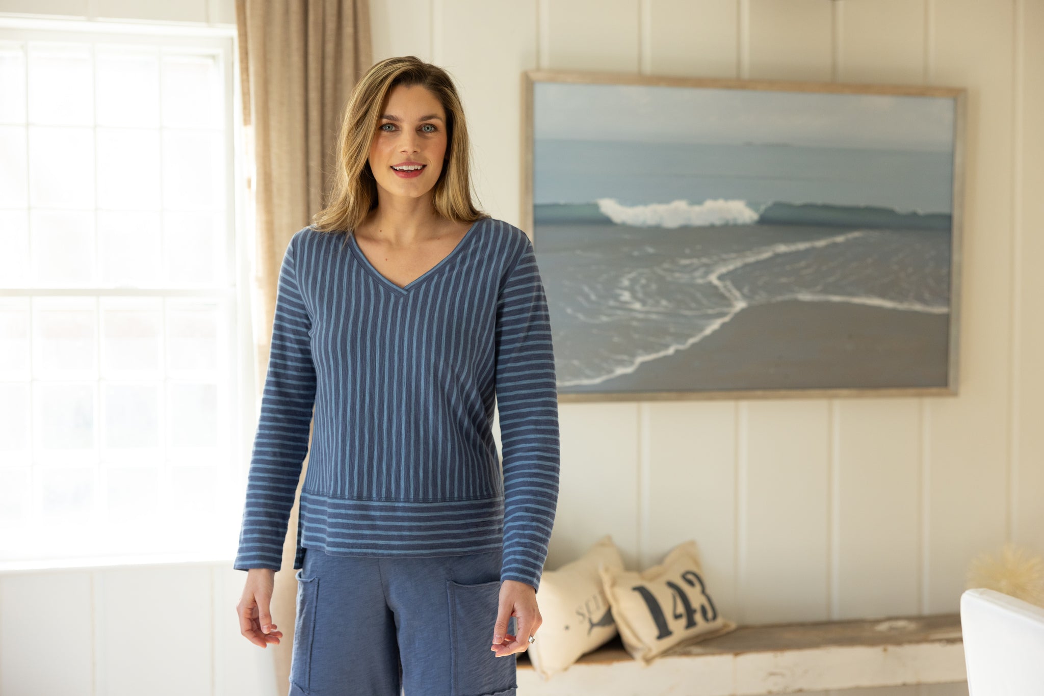Woman wearing a blue striped sweater in a room with a painting of a beach scene.