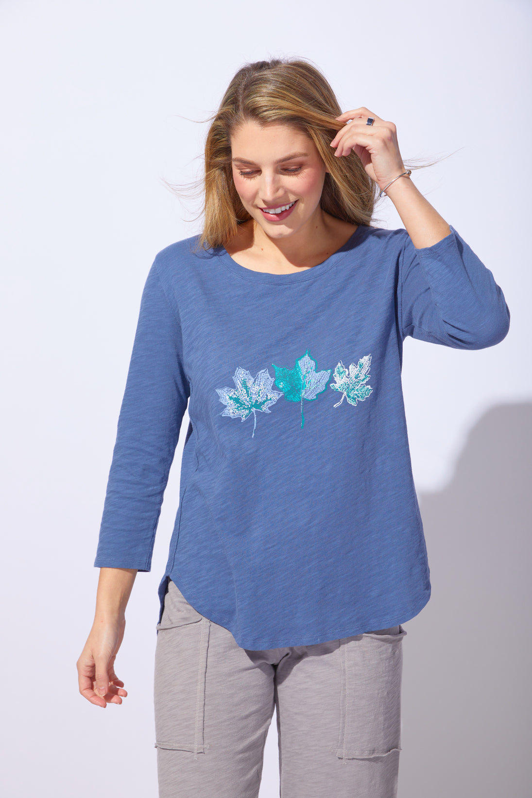 Woman wearing a blue long-sleeve shirt with leaf designs on a white background