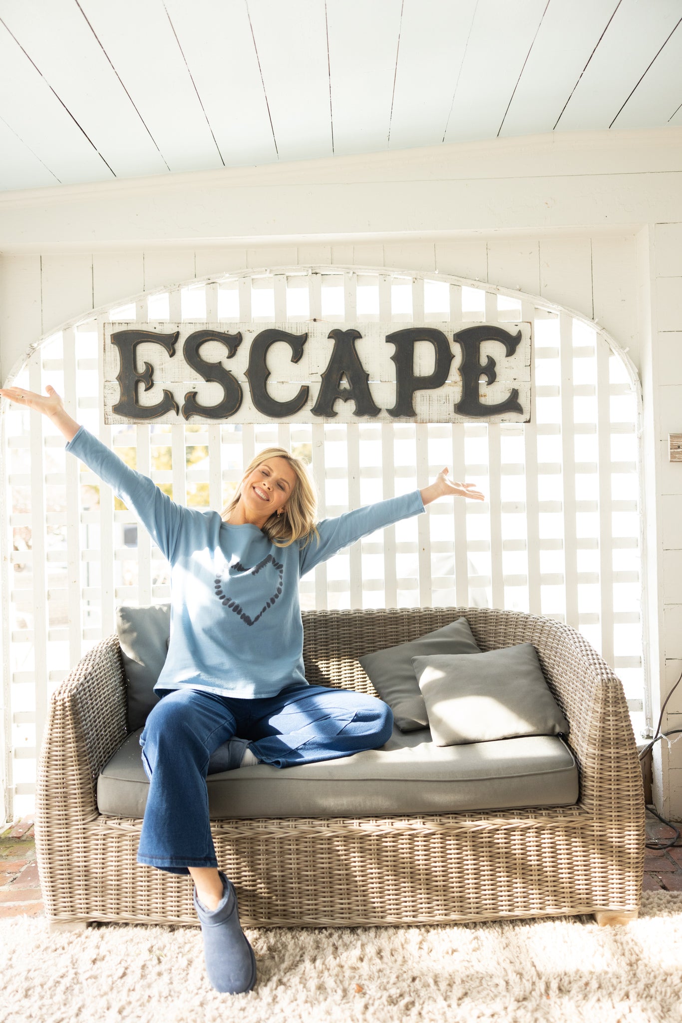 Woman sitting on a couch with arms outstretched in front of a wall with the word 'ESCAPE'.