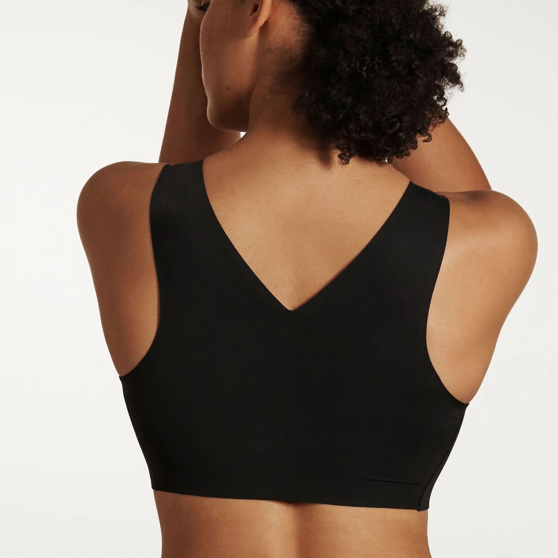 Woman wearing the Evelyn & Bobbie Defy Bra in Black, no wire pullover bra, against a white background, back view.