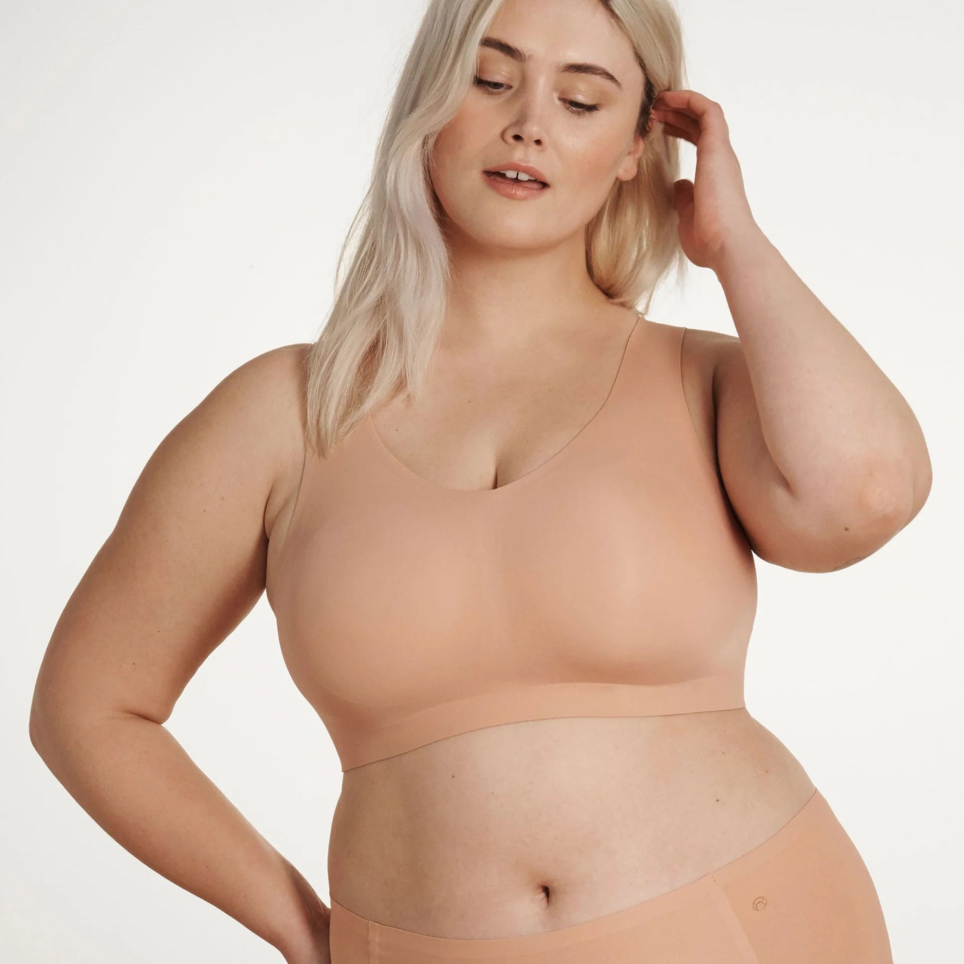 Woman wearing the Evelyn & Bobbie Defy bra in Himalayan Salt, light pinkish beige no wire pullover bra, against a white background front view.