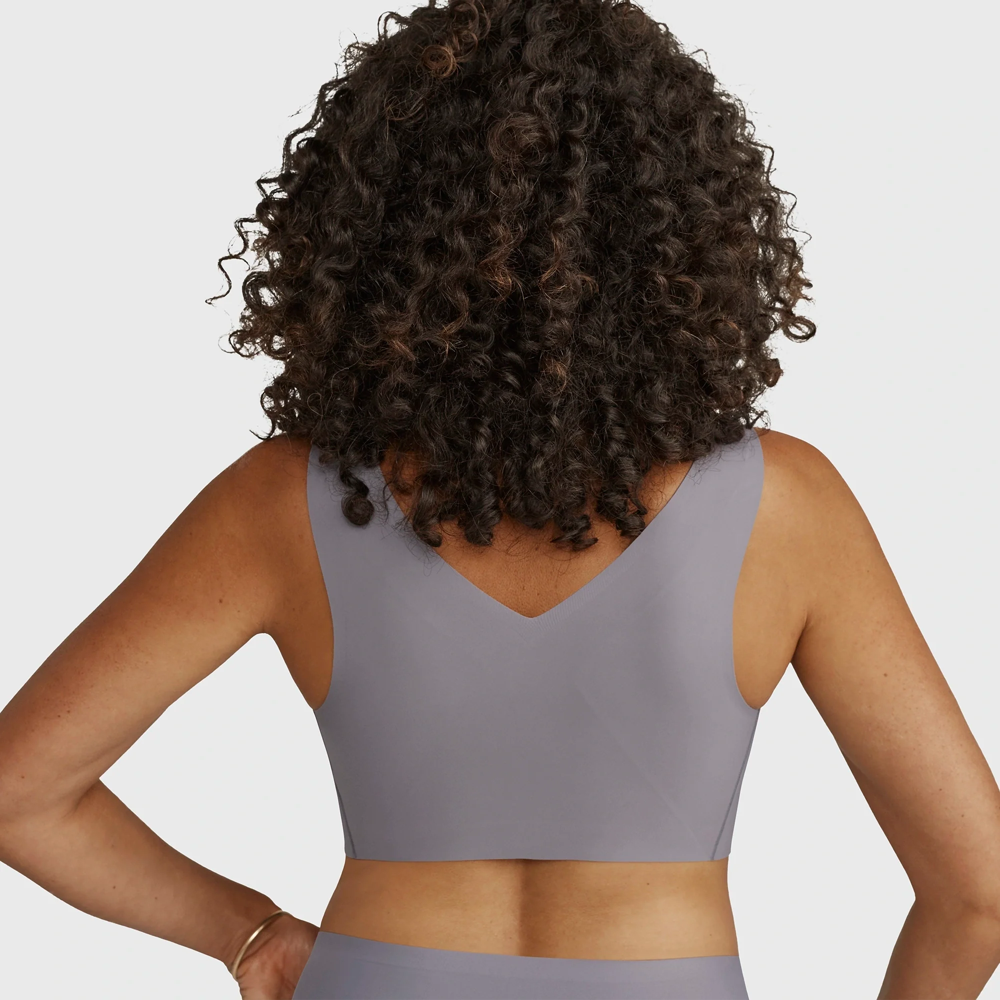 Woman wearing the Evelyn Bobbie Defy Bra in London Fog, light grey no wire bra, on a white background, view of her back smooth band.