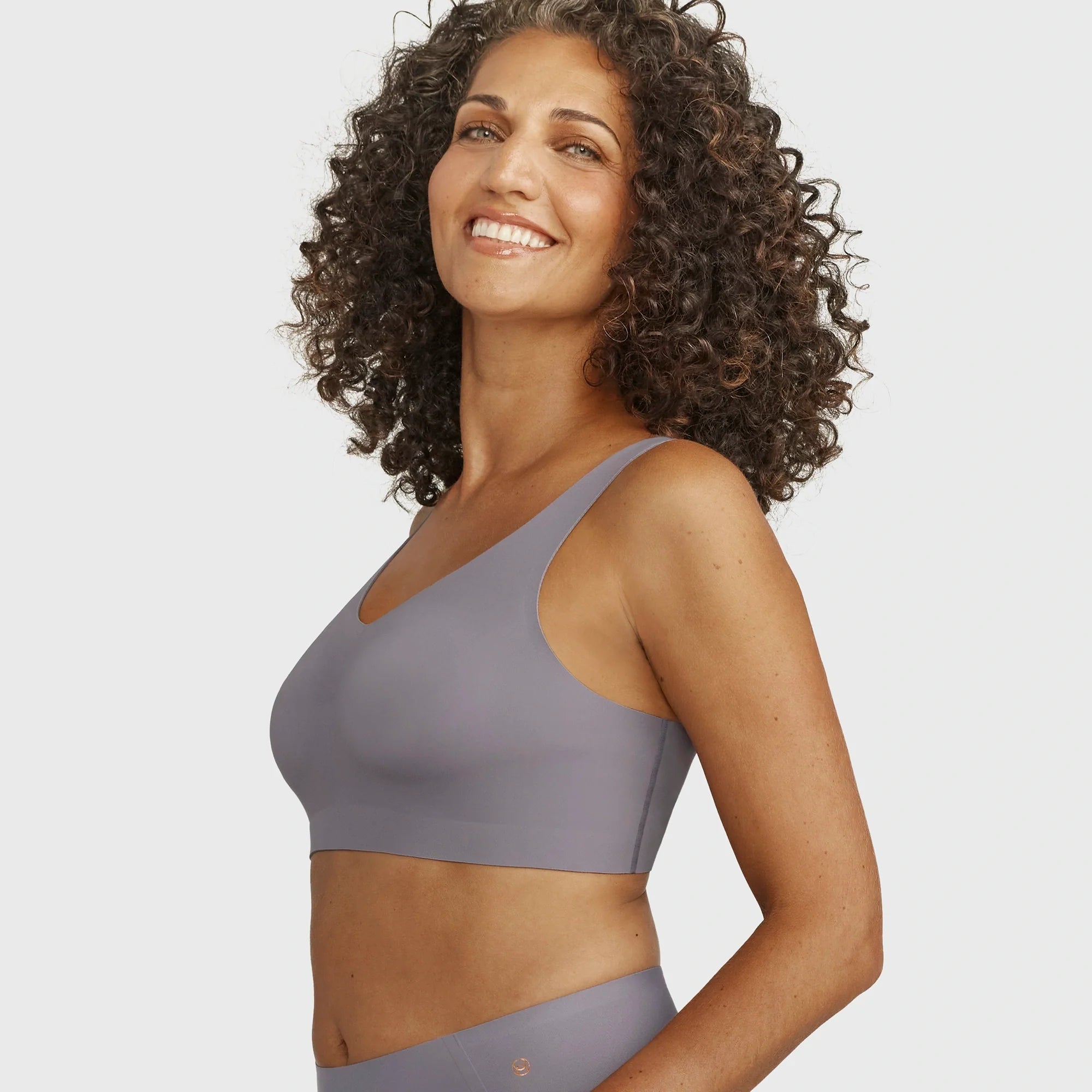Woman wearing the Evelyn Bobbie Defy Bra in London Fog, light grey no wire bra, on a white background.