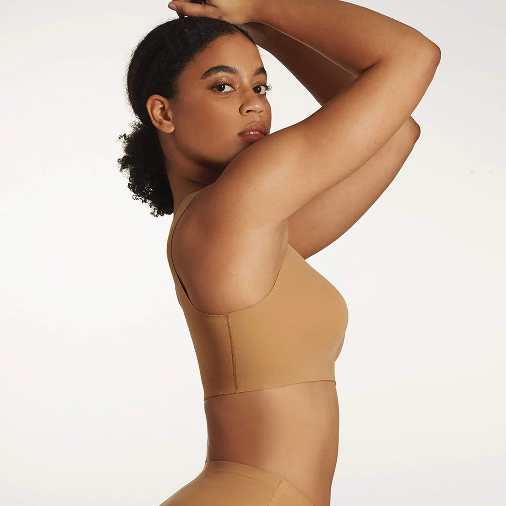 Woman wearing the Evelyn & Bobbie Defy Bra in Mica, light tan no wire pullover bra, against a white background, side view.