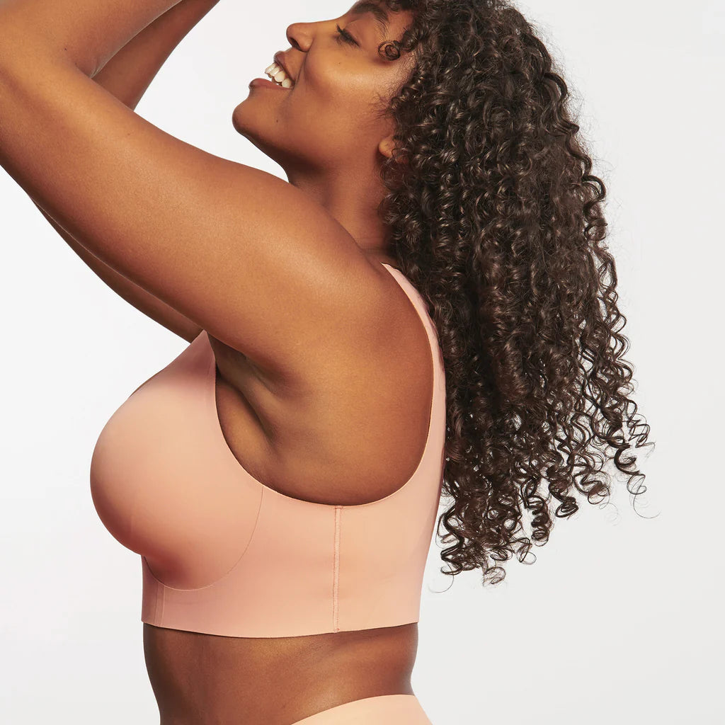 Woman wearing Evelyn & Bobbie Evelyn Bra in Himalayan Salt, light pink no wire pullover bra, against a white background, side view.