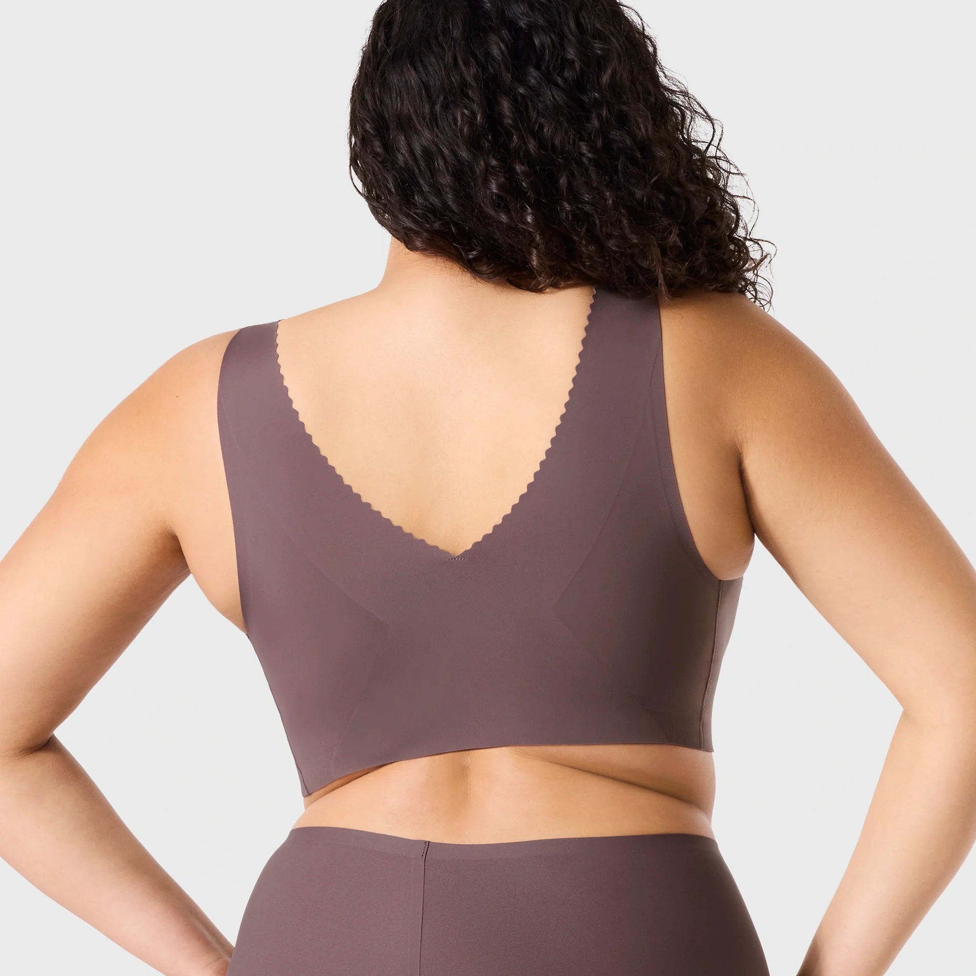 Woman wearing Evelyn & Bobbie Evelyn Bra in Thistle, dark mauve no wire pullover bra, against a white background, back view.