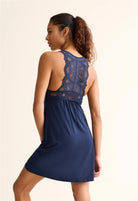 A woman wearing a blue chemise with a lace back against a white background
