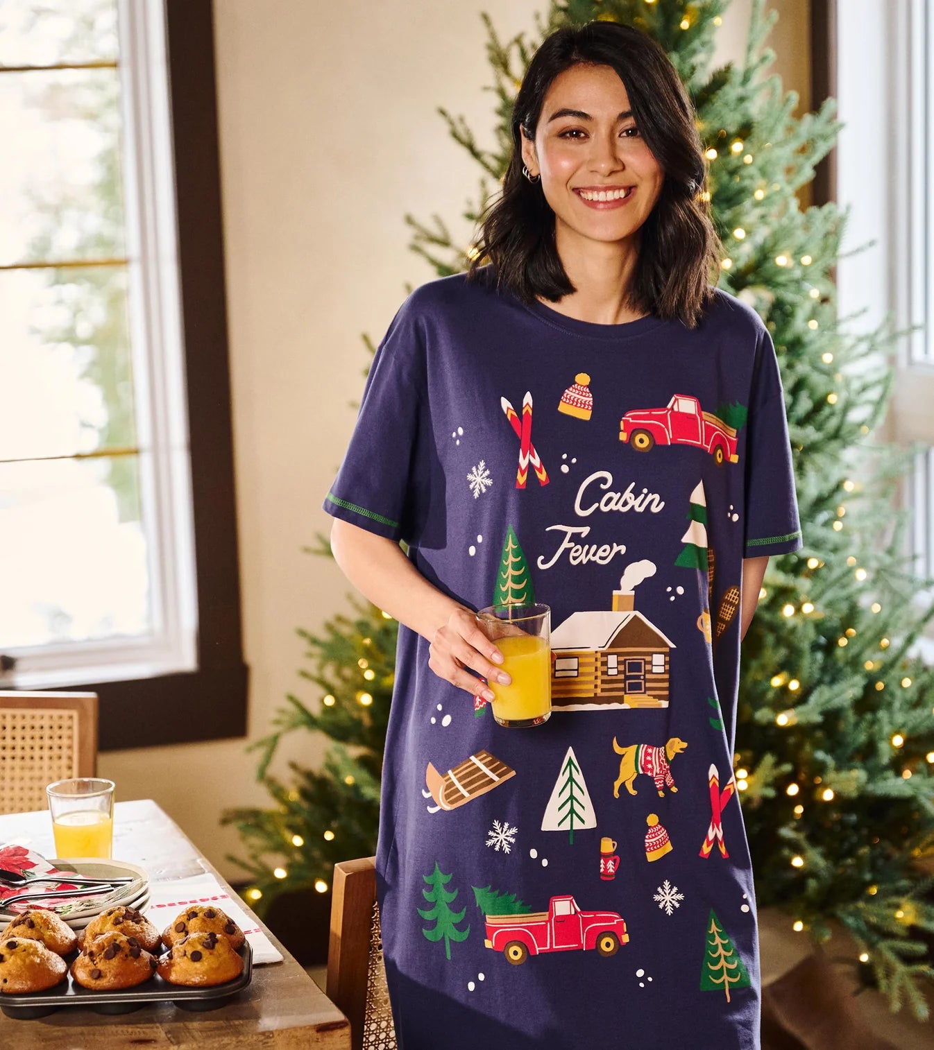 Woman wearing a 'Cabin Fever' themed nightshirt in a festive room with Christmas trees.