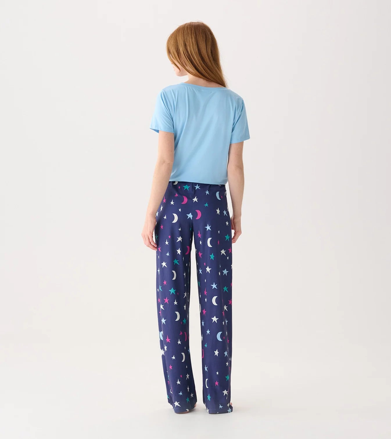 Person wearing a light blue t-shirt and navy pajama pants with star and moon pattern on a white background