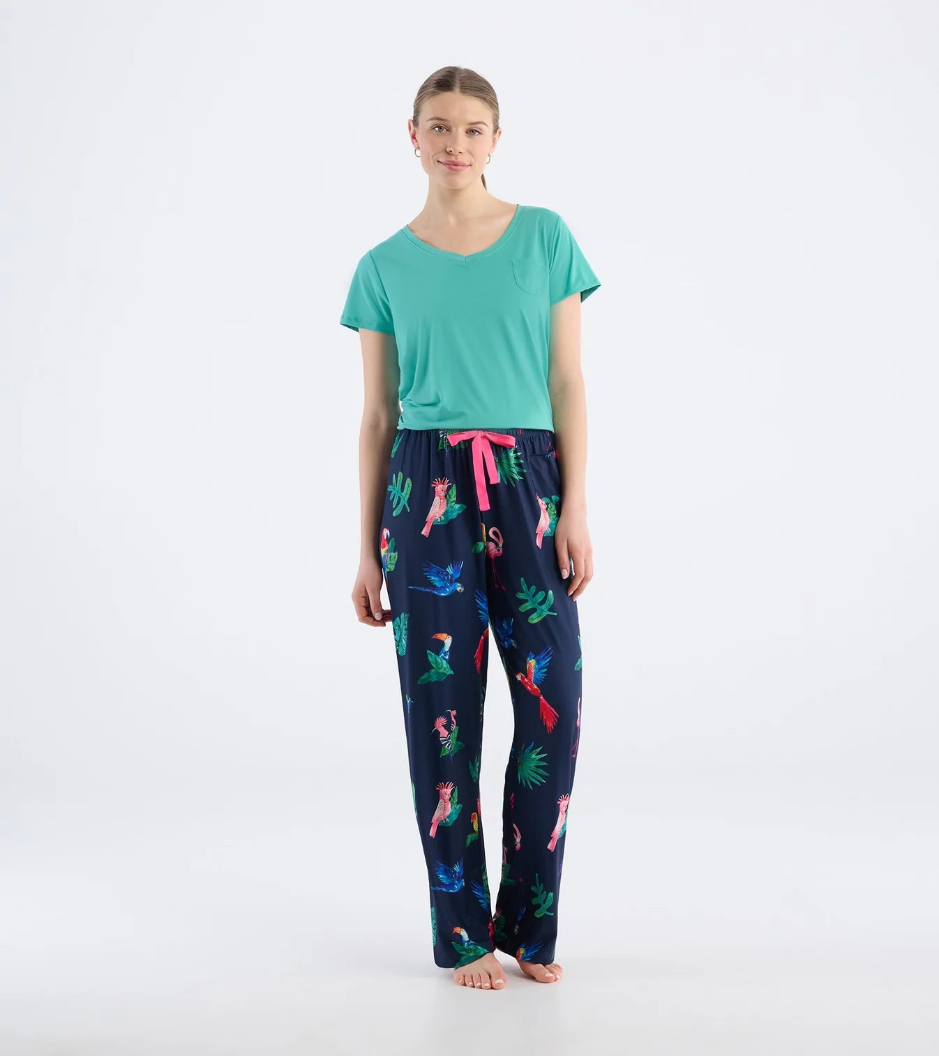 Woman wearing a green t-shirt and navy pajama pants with colorful parrot pattern on a white background