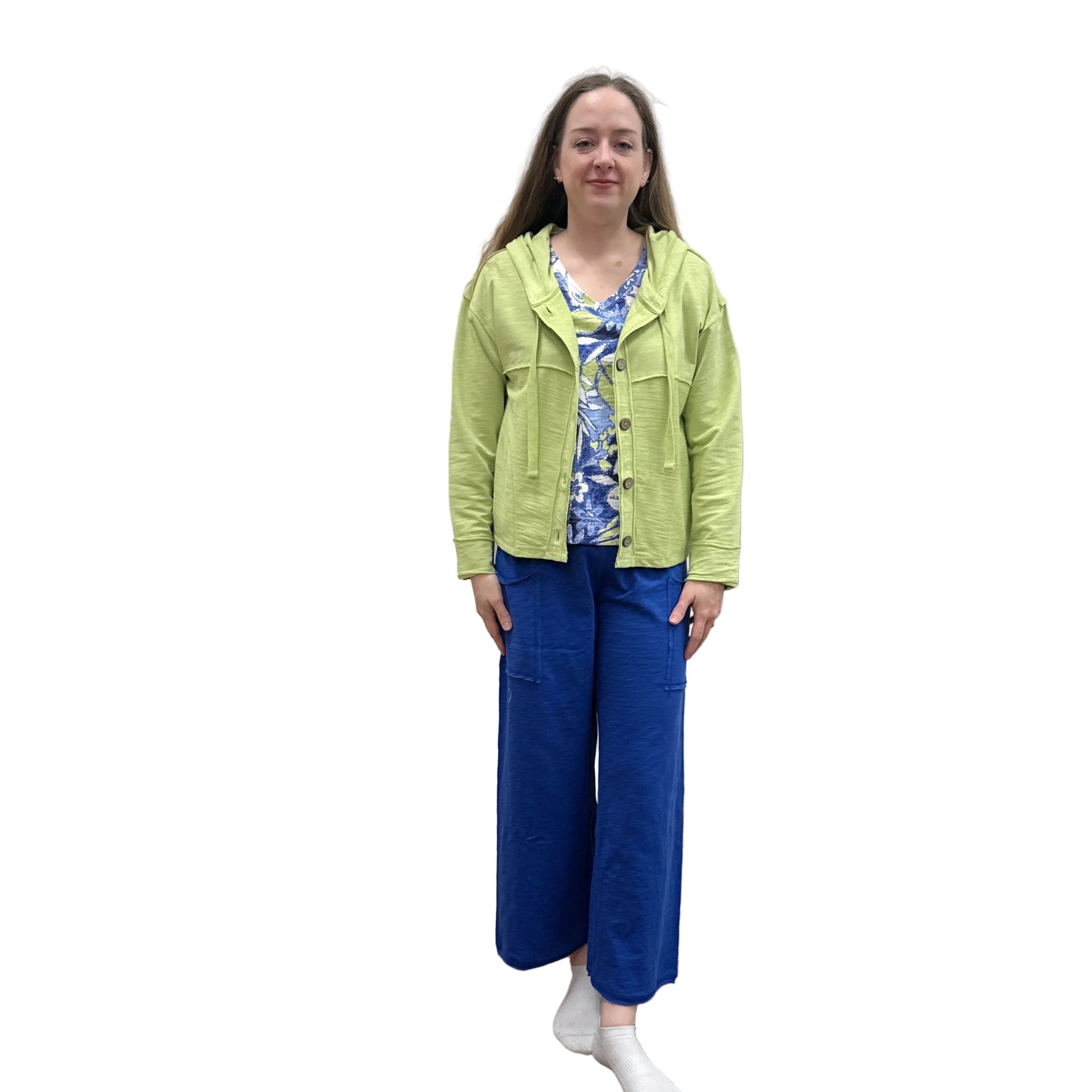 Person wearing a kiwi green Cruising Hoodie jacket and blue pants standing against a plain wall.