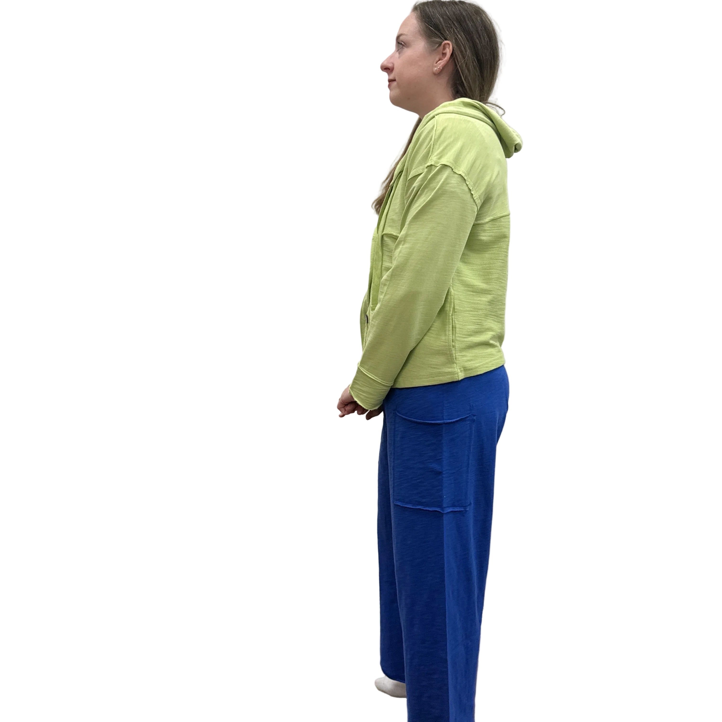 Person wearing a kiwi green Cruising Hoodie jacket and blue pants standing against a plain wall.