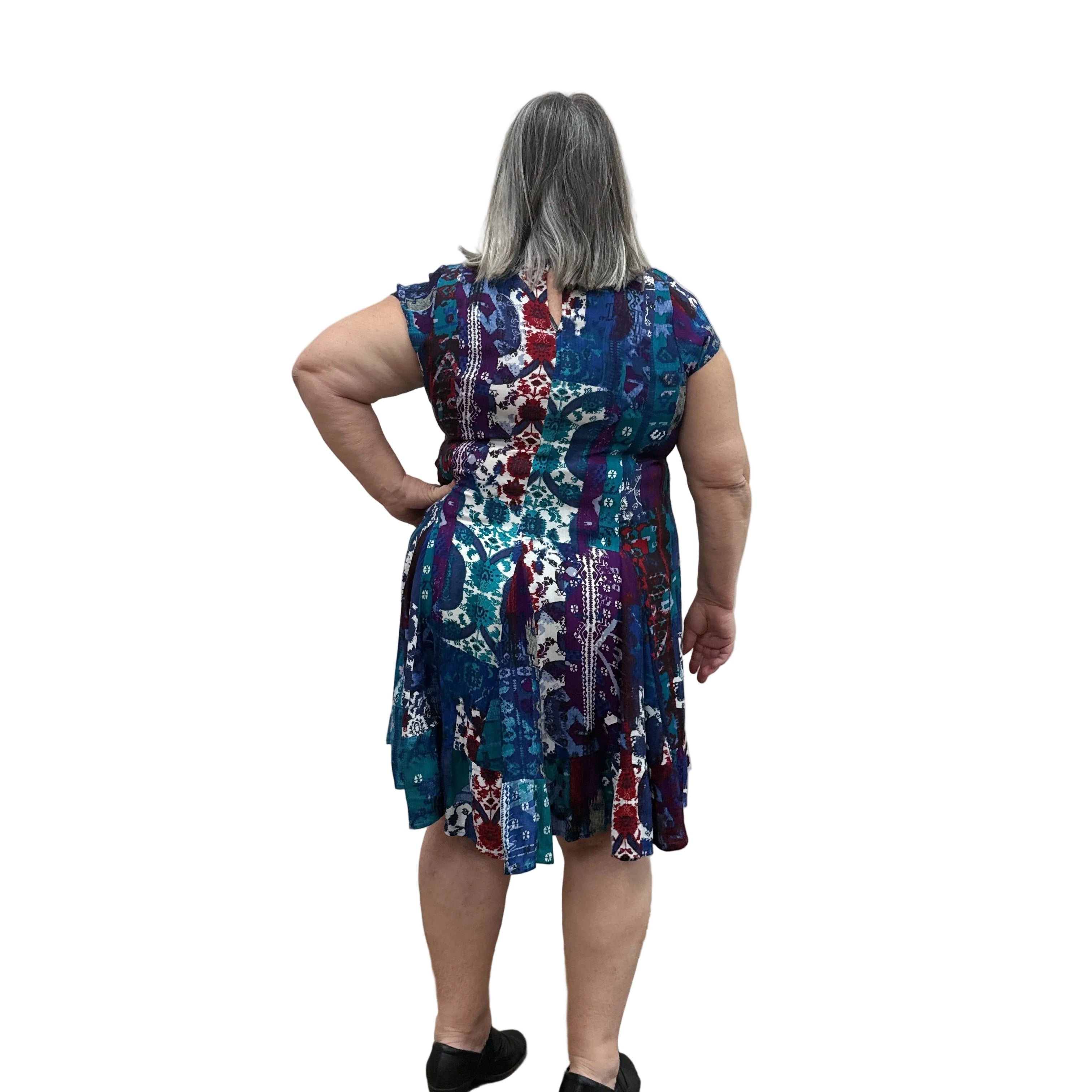 Woman wearing the Papa Indigo Mosaic Breeze patterned dress against a white background, facing the wall to see the back of the dress.