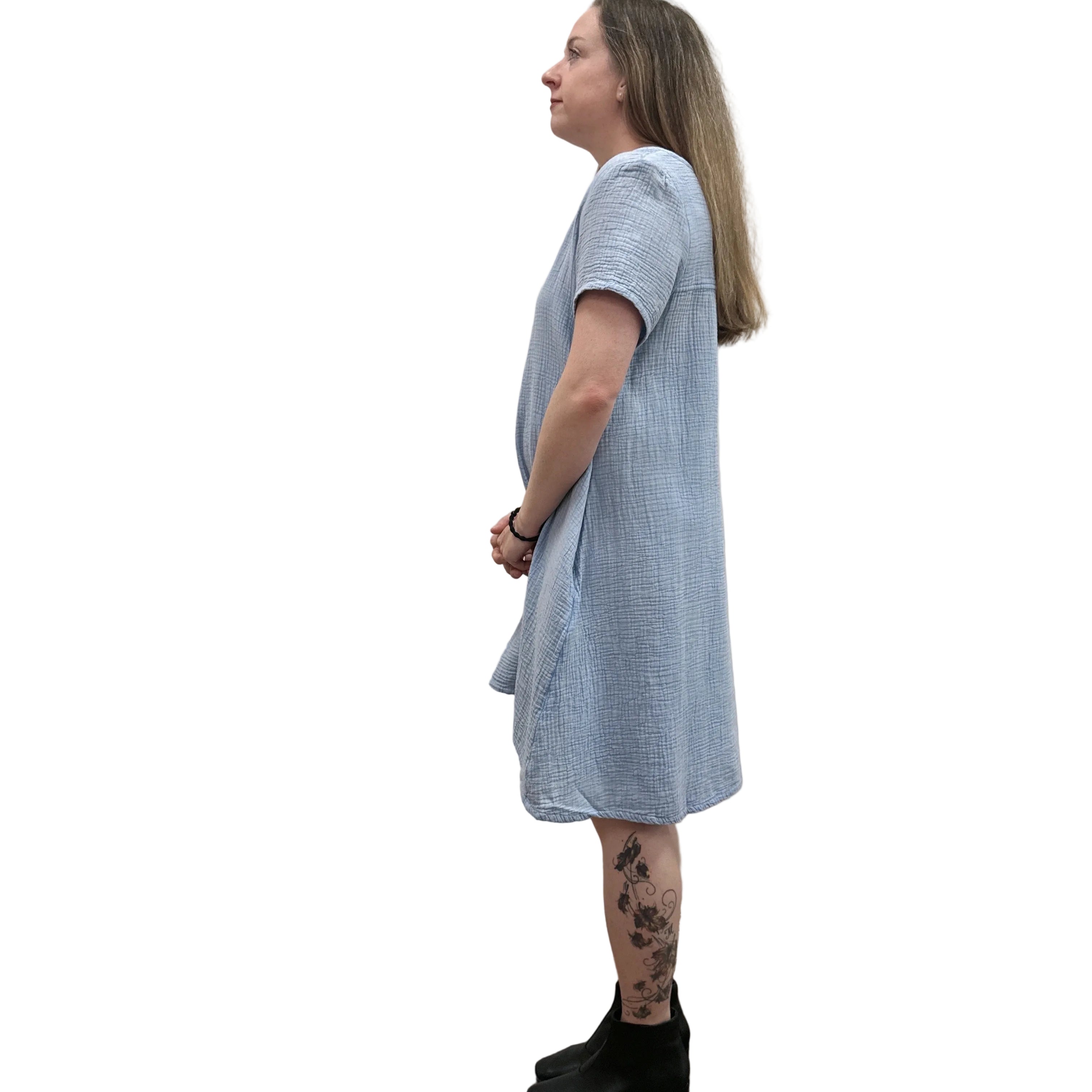 Woman wearing a light blue Papa Passport dress against a plain wall, side view.